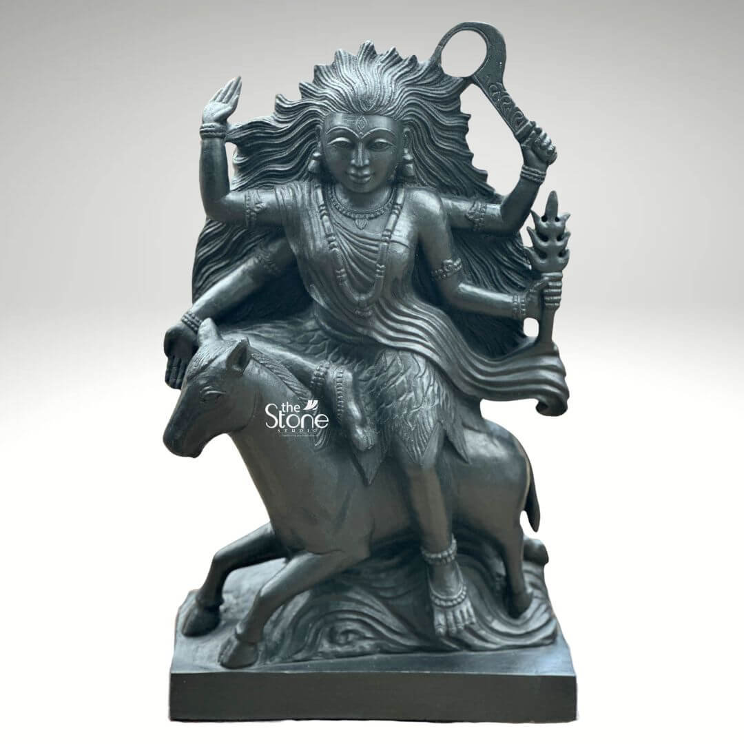 Black Stone Kaalratri Statue 15" 1 A powerful Black Stone Kaalratri statue sculpted with dynamic energy stands prominently against a stark white background. This fierce manifestation of the Divine Mother one of the Navadurga is depicted riding a horse symbolizing her swift action and determination to destroy evil. Her hair appears to be unbound and flowing wildly emphasizing her formidable and untamed nature true to her name the night of blackness. The black stone statue of Kaalratri is rich with symbolic details. The goddess is multi-armed with her hands wielding various weapons and implements; one hand prominently holds a saber or sword-like weapon aloft while another grasps a trident or a similar fiery object. Her expression though intense also conveys a sense of divine purpose. She is adorned with sculpted jewelry including necklaces and bangles which contrast with her fierce form. The horse she rides is captured mid-action its legs seemingly galloping through waves or clouds carved to enhance the sense of movement and power. The deep uniform black of the stone enhances the statue's dramatic and revered presence. This striking black stone Kaalratri statue is an excellent visual for an article detailing such powerful deities. The choice of black stone perfectly embodies her dark destructive aspect against evil while the intricate carving of her wild hai weapons and dynamic pose on the horse conveys her relentless energy. The statue is a compelling representation of Kaalratri's role in vanquishing fear and ignoranc making it a significant piece for devotees and art enthusiasts alike.