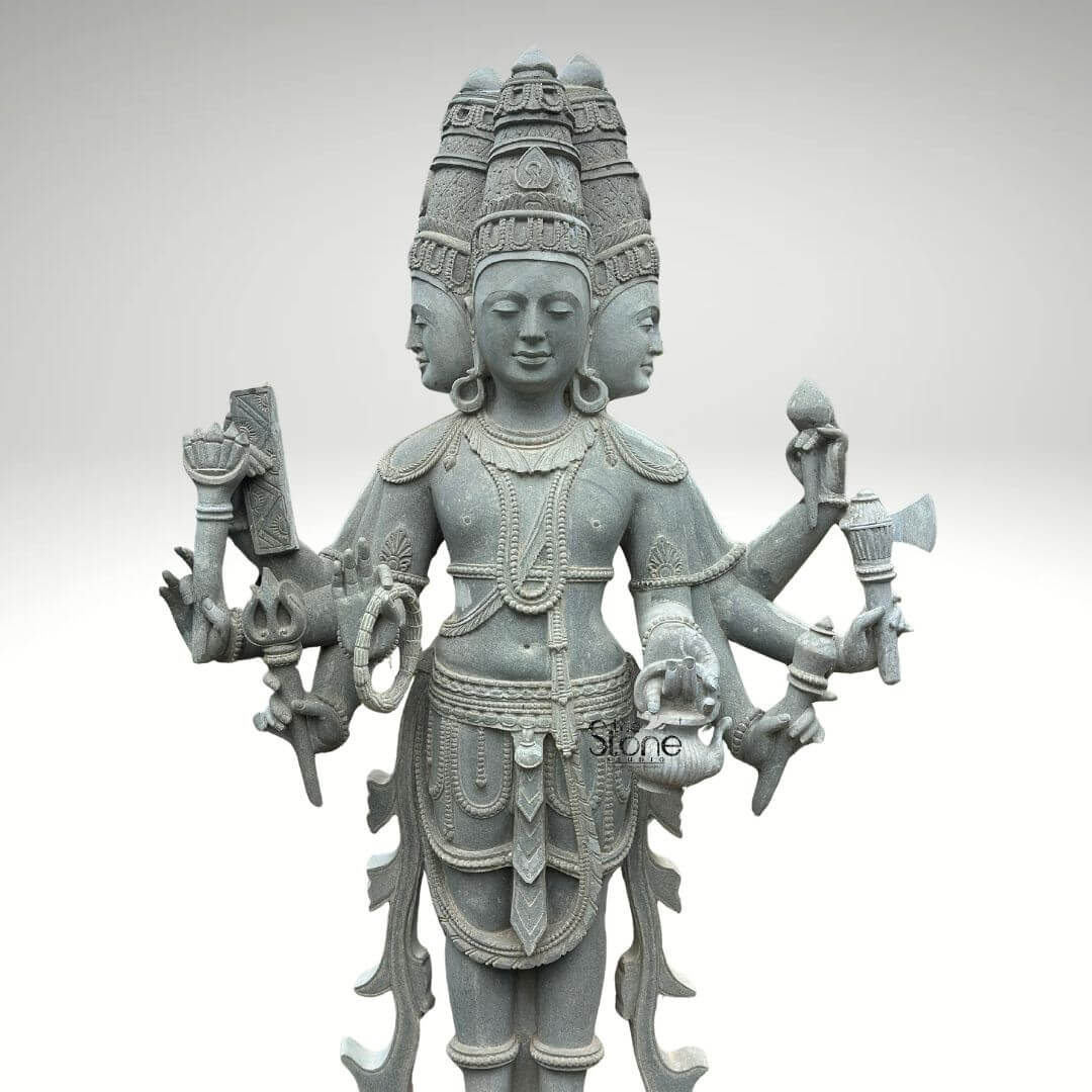 Brahma Stone Statue 7ft 5 A magnificent 7-foot greystone Brahma stone idol is presented in a stately front-facing view against a plain light background emphasizing its grandeur and intricate craftsmanship. The statue depicts Lord Brahma the creator god in a standing posture with his characteristic four heads symbolizing his omnipresence and knowledge of the four Vedas. The natural grey tones and subtle textures of the stone lend an ancient and dignified quality to this impressive idol highlighting its detailed carvings. Lord Brahma is meticulously carved with his four serene and contemplative faces each adorned with an elaborate crown and facing the cardinal directions. He is richly adorned with multiple necklaces armlets and a sacred thread all finely detailed. In his multiple hands he holds his traditional attributes including a sruva (ladle) or rosary a kamandalu and a puskara symbolizing his role in creation and knowledge. His attire is elegantly draped with intricate patterns on his lower garment and decorative elements around his waist. He stands barefoot conveying humility despite his divine stature. The high level of detail in the carving from the delicate facial features to the intricate jewelry speaks to exceptional artistry. This 7-foot greystone Brahma stone idol is a profound representation of creation, wisdom and cosmic knowledge making it a powerful and auspicious addition to any temple or significant spiritual space. The exceptional craftsmanship in natural greystone not only makes it a visually striking piece but also imbues it with deep cultural and religious significance. This exquisitely detailed statue serves as a commanding focal point for devotion and prayer radiating positive energy and ancient wisdom to all who venerate it.