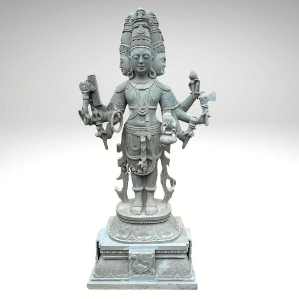 A magnificent 7-foot greystone Brahma statue is presented in a stately front-facing view against a plain light background emphasizing its grandeur and intricate craftsmanship. The statue depicts Lord Brahma the creator god in a standing posture with his characteristic four heads symbolizing his omnipresence and knowledge of the four Vedas. The natural grey tones of the stone lend an ancient and dignified quality to this impressive statue highlighting its detailed carvings. Lord Brahma is meticulously carved with his four faces each serene and contemplative facing the cardinal directions. He is adorned with an elaborate crown multiple necklace armlets and a sacred thread all finely detailed. In his multiple hands he holds his traditional attributes including a sruva or rosary a kamandalu and a puskara symbolizing his role in creation and knowledge. His attire is elegantly draped and he stands barefoot on a lotus pedestal which in turn rests on a multi-tiered intricately carved base featuring smaller decorative elements and possibly mythical creatures. This 7-foot greystone Brahma statue is a profound representation of creation wisdom and cosmic knowledge making it a powerful and auspicious addition to any temple or significant spiritual space. The exceptional craftsmanship in natural greystone not only makes it a visually striking piece but also imbues it with deep cultural and religious significance. This exquisitely detailed statue serves as a commanding focal point for devotion and prayer radiating positive energy and ancient wisdom to all who venerate it.