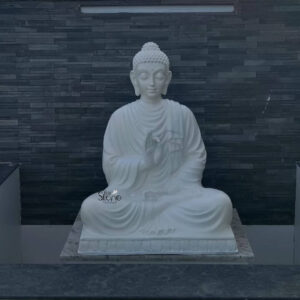 A serene 4-foot Buddha fiber statue finished in a pristine white is depicted seated in a meditative pose against a dark textured wall creating a striking contrast that highlights its tranquil presence. The statue portrays the Buddha in Padmasana with his right hand in the Vitarka Mudra symbolizing teaching and intellectual discussion while his left hand rests in his lap palm upwards signifying meditation. This large pristine white Buddha statue is a profound symbol of peace and enlightenment ideally suited for a public or private setting in Nagapattinam Tamil Nadu. The Buddha's face is carved with an expression of profound serenity and wisdom with downcast eyes suggesting deep contemplation. His ushnisha and tightly curled hair are meticulously detailed indicative of a finely crafted piece. The flowing drapery of his robes is rendered with soft natural folds adding to the realism and grace of the figure. The statue sits on a simple rectangular base which in turn rests on a light-colored possibly marble platform providing a dignified foundation for the revered figure. The dark stone-like wall behind it provides a dramatic and elegant backdrop allowing the white statue to truly stand out. This 4-foot Buddha fiber statue is an exceptional piece that brings an immediate sense of calm and spiritual harmony to any environment. Its durable fiber construction ensures longevity and suitability for various settings while its large size makes it a commanding and inspiring presence. As a symbol of enlightenment and peace this Buddha statue is not only an artistic masterpiece but also a significant spiritual icon inviting contemplation and fostering a tranquil atmosphere whether in a temple garden or large indoor space in Nagapattinam.
