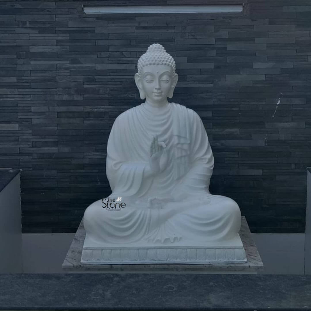 Fiber Buddha Statue 4 feet 3 A serene 4-foot Buddha fiber statue finished in a pristine white is depicted seated in a meditative pose against a dark textured wall creating a striking contrast that highlights its tranquil presence. The statue portrays the Buddha in Padmasana with his right hand in the Vitarka Mudra symbolizing teaching and intellectual discussion while his left hand rests in his lap palm upwards signifying meditation. This large pristine white Buddha statue is a profound symbol of peace and enlightenment ideally suited for a public or private setting in Nagapattinam Tamil Nadu. The Buddha's face is carved with an expression of profound serenity and wisdom with downcast eyes suggesting deep contemplation. His ushnisha and tightly curled hair are meticulously detailed indicative of a finely crafted piece. The flowing drapery of his robes is rendered with soft natural folds adding to the realism and grace of the figure. The statue sits on a simple rectangular base which in turn rests on a light-colored possibly marble platform providing a dignified foundation for the revered figure. The dark stone-like wall behind it provides a dramatic and elegant backdrop allowing the white statue to truly stand out. This 4-foot Buddha fiber statue is an exceptional piece that brings an immediate sense of calm and spiritual harmony to any environment. Its durable fiber construction ensures longevity and suitability for various settings while its large size makes it a commanding and inspiring presence. As a symbol of enlightenment and peace this Buddha statue is not only an artistic masterpiece but also a significant spiritual icon inviting contemplation and fostering a tranquil atmosphere whether in a temple garden or large indoor space in Nagapattinam.