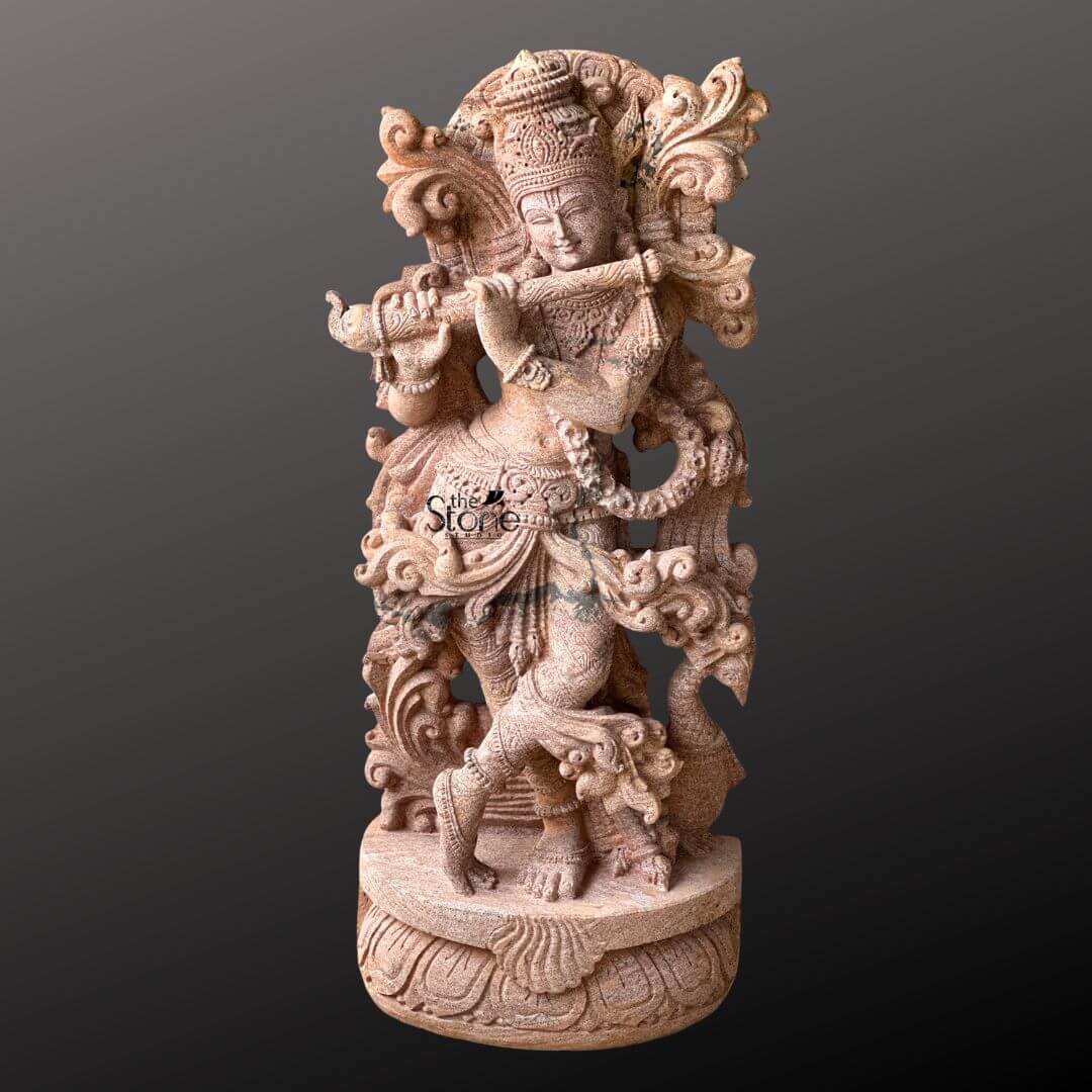 Standing Krishna Stone Statue with Flute 3.5ft 2 A beautifully rendered 3.5-foot decorative Krishna stone sculpture crafted from sandstone stands majestically against a muted dark background. The deity is captured in a dynamic and graceful posture playing his bansuri with his body subtly angled in the classic Tribhanga pose. His right leg is crossed in front of his left indicating movement and a captivating dance-like quality while his hands are positioned to hold the flute suggesting an enchanting melody. The sandstone sculpture is rich with intricate details showcasing the artistry involved in its creation. Krishna's head is adorned with an elaborate crown likely featuring the iconic peacock feather a symbol deeply intertwined with his persona. His divine form is embellished with carved jewelry including multiple necklaces armbands waist chains and anklets all meticulously etched into the stone. The folds of his dhoti and the ornate sashes are sculpted with a sense of fluidity enhancing the sculpture's decorative appeal. Behind Krishna an ornate arch or halo possibly depicting natural elements like foliage or peacock feathers frames him adding to the overall grandeur. This 3.5-foot sandstone Krishna sculpture is a perfect example of decorative stone artistry as featured in an article about such pieces. The warm earthy tones of the sandstone naturally highlight the intricate carvings and bring out the expressive qualities of the sculpture. Its elegant posture divine adornments and the timeless act of playing the flute make it a captivating and culturally significant decorative item capable of gracing any space with beauty serenity and spiritual resonance.