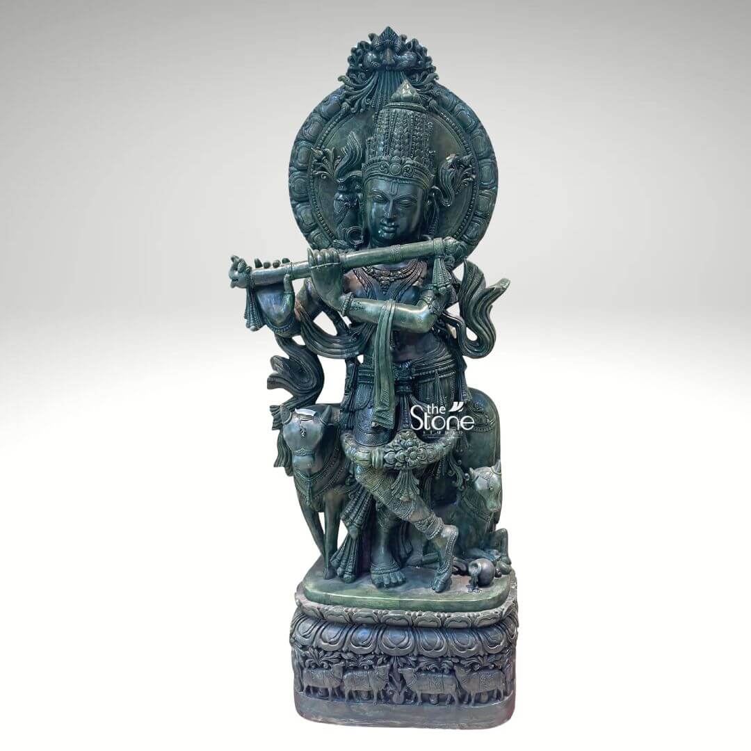Green Stone Krishna with Cow Statue 4ft 2 A magnificent Gopal Krishna Stone Statue meticulously carved from greenstone stands prominently against a clean white background showcasing exquisite detail and artistry. Lord Krishna in his form as Gopal is depicted in his iconic Tribhanga pose gracefully playing his flute his body angled with a serene expression. Beside him a cow and a calf are intricately carved reflecting his identity as a divine cowherd an essential aspect of the Gopal Krishna theme. The greenstone material gives the entire sculpture a distinctive earthy and revered appearance. The greenstone Gopal Krishna statue is rich with traditional ornamentation. Krishna wears an elaborate crown likely adorned with a peacock feather a symbol strongly associated with him. His form is embellished with finely carved jewelry including necklaces armlets waistbands and anklets. The flowing drapery of his dhoti and sashes adds to the dynamic quality of the pose. Behind Krishna a circular aureole or halo frames his head often symbolizing divinity and a larger ornate arch rises above featuring intricate patterns. The cow and calf are rendered with gentle expressions symbolizing prosperity and devotion and they are surrounded by carved foliage and other natural elements. This Greenstone Gopal Krishna statue is an ideal visual for an article detailing such divine sculptures. The statue rests on a multi-tiered intricately carved base which features a band of smaller animal figures possibly more cows further enhancing the pastoral theme. The harmonious composition of Krishna the cow and the detailed base in greenstone creates a powerful and spiritually uplifting piece embodying devotion divine love and the sacred bond between Krishna and nature perfect for a temple or a home seeking a touch of spiritual grace associated with Gopal Krishna.