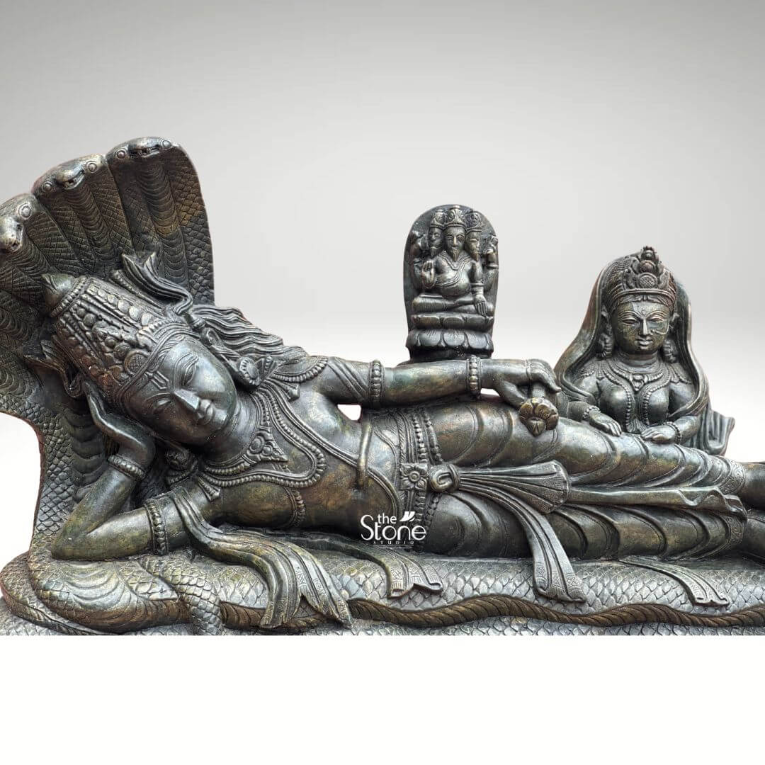 Ananta Shayana Vishnu Statue 20" 5 A magnificent green stone sculpture depicts Lord Vishnu reclining on the cosmic serpent Sheshnag a powerful and iconic image of cosmic preservation and creation in Hindu mythology. The statue captures Vishnu in his Ananta Shayana posture signifying his cosmic sleep during the dissolution of the universe. The deep rich green of the stone possibly a dark serpentine or steatite imbues the sculpture with an ancient and mystical aura highlighting the intricate details of the figures and the dynamic flow of the serpent's coils. Lord Vishnu is carved with serene features his eyes gently closed in cosmic slumber his head resting on his right arm. He is adorned with an elaborate crown necklaces armlet and a sacred thread all meticulously detailed. From his navel emerges a lotus flower upon which sits a smaller idol of Brahma the creator god symbolizing the cyclical nature of creation as Brahma emerges from Vishnu's cosmic dream. To Vishnu's right seated reverently at his feet is Goddess Lakshmi his consort depicted with equally elaborate adornments and a pose of devoted service. The multi-headed Sheshnag forms a grand canopy over Vishnu its scales and coils intricately rendered. This green stone sculpture of Lord Vishnu reclining on Sheshnag is a profound representation of cosmic order preservation and the continuous cycle of time. The exceptional detail and the choice of green stone often associated with spiritual balance and renewal enhance its spiritual potency. This statue embodying the very essence of Vishnu's role as the preserver is an impressive and deeply meaningful artifact ideal for a grand temple a prominent home altar or as a centerpiece in a spiritual garden inviting contemplation and reverence for the divine cosmic dance.