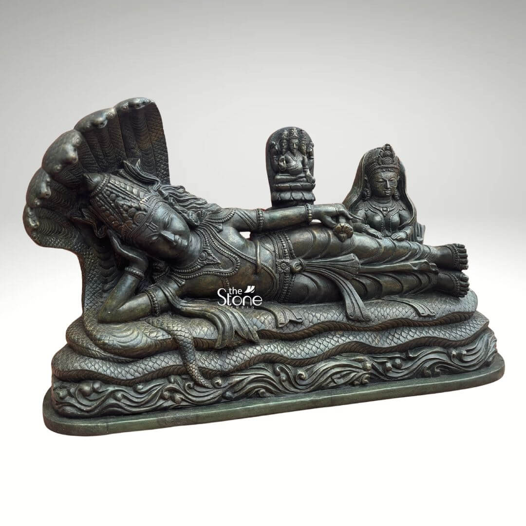 Ananta Shayana Vishnu Statue 20" 6 A magnificent green stone statue of Lord Vishnu Narayana reclining on the cosmic serpent Sheshnag is presented in a detailed slightly elevated view making it an ideal centerpiece for a home temple. The statue beautifully captures the iconic Ananta Shayana pose symbolizing cosmic rest and the continuous cycle of creation and dissolution. The deep verdant green of the stone possibly a dark serpentine or soapstone enhances the antique and sacred aesthetic bringing out the intricate carvings and the profound narrative embedded within the sculpture. Lord Vishnu is depicted in a state of serene cosmic slumber his head gently supported by his right arm with an expression of profound peace. He is adorned with an elaborate crown, necklaces armlets and a gracefully draped dhoti, all carved with meticulous precision. The multi-headed Sheshnag coils beneath him, its numerous hoods fanning out to form a protective canopy over Vishnu's head. From Vishnu's navel, a small lotus rises bearing a miniature figure of Brahma the creator god illustrating the universe's cyclical emergence from Vishnu's dream. To Vishnu's right seated attentively is Goddess Lakshmi his divine consort her form equally adorned and sculpted with reverence massaging his feet. This green stone Vishnu Narayana statue is a powerful and sacred representation of preservation cosmic order and the cyclical nature of time in Hindu mythology perfectly suited for a home temple. The exceptional detail and the choice of green stone often associated with spiritual balance and renewal enhance its spiritual potency. This exquisitely detailed statue is an impressive and deeply meaningful artifact inviting contemplation and reverence for the divine cosmic dance and enriching any home temple with its profound cultural and religious significance.