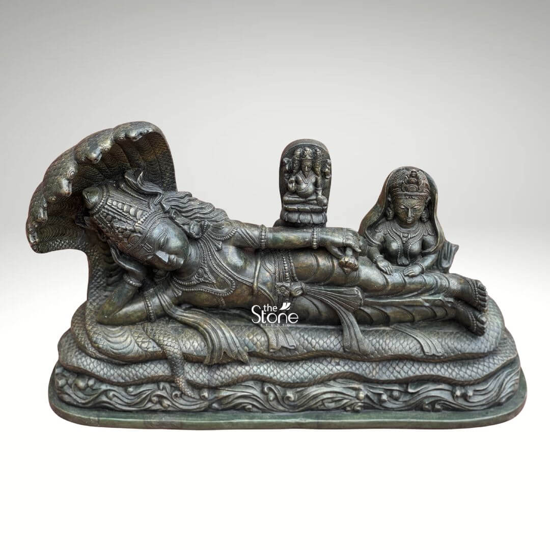 Ananta Shayana Vishnu Statue 20" 7 A magnificent hand-carved green stone statue depicts Lord Vishnu and Goddess Lakshmi in the iconic Ananta Shayana pose with Vishnu reclining on the cosmic serpent Sheshnag. This intricate sculpture designed to be a centerpiece showcases the profound narrative of cosmic preservation and divine companionship. The deep rich green of the stone likely soapstone or a similar fine-grained metamorphic rock lends an ancient and spiritual gravitas to the meticulously detailed figures and the dynamic flow of the serpent's coils highlighting the artisanal skill. Lord Vishnu is rendered in a state of serene cosmic slumber his head gently supported by his right arm with an expression of ultimate tranquility that conveys universal peace. He is lavishly adorned with traditional ornaments including a majestic crown multiple necklaces intricate armlets and a gracefully draped dhoti all carved with remarkable precision. The multi-headed Sheshnag forms a majestic canopy over Vishnu's head its scales and undulating body forming the base. From Vishnu's navel a delicate lotus emerges bearing a miniature figure of Brahma the creator god symbolizing the universe's cyclical creation. To Vishnu's right seated attentively is Goddess Lakshmi his divine consort her form equally adorned and sculpted with reverence completing the sacred tableau. This hand-carved green stone Vishnu Lakshmi statue is a powerful and sacred representation of preservation prosperity and cosmic order in Hindu mythology. The choice of green stone often associated with natural harmony growth and spiritual renewal significantly enhances the idol's profound symbolism and aesthetic appeal. This exquisitely detailed statue is an impressive and deeply meaningful artifact ideal for a grand home temple or a prominent spiritual display offering a rich source of contemplation and devotion and enriching any space with its deep cultural and religious resonance.