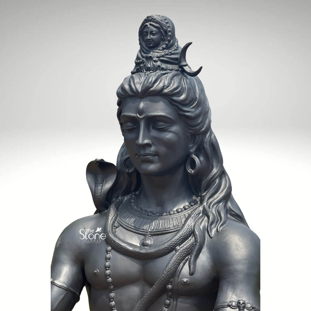 6 Feet Meditating Lord Shiva Statue 7 A close-up high-detail image of a handcrafted 6-foot Fibre Lord Shiva Murti finished to resemble antique metal focuses on the deity's upper body and intricate iconography. The statue depicts Lord Shiva with his eyes gently closed in deep meditation radiating an aura of profound tranquility cosmic power and divine wisdom. This large-scale fiber Shiva Murti is an impressive and inspiring piece showcasing meticulous craftsmanship and spiritual depth. Lord Shiva's face is sculpted with remarkable serenity featuring a prominent tilak on his forehead. His long flowing matted hair is elaborately piled high adorned with a crescent moon and a miniature figure of Goddess Ganga symbolizing the sacred river's descent. A lifelike cobra gracefully coils around his neck and multiple rudraksha bead malas drape across his chest and muscular torso along with other ornate necklaces and armbands. The metallic finish of the fiber material captures the subtle play of light and shadow highlighting every intricate detail of the carving from the texture of his hair to the smooth contours of his skin. This handcrafted 6-foot Fibre Lord Shiva Murti is a powerful representation of the ultimate reality the destroyer of evil and the source of all yoga and meditation. The exceptional artistry in fiber allows for such intricate detailing and a commanding yet peaceful presence making it a visually striking and spiritually significant artifact. This Murti not only serves as a focal point for devotion and meditation but also as a majestic piece of art that radiates peace strength and cosmic energy enriching any space with its profound cultural and religious resonance truly capturing the essence of Lord Shiva.