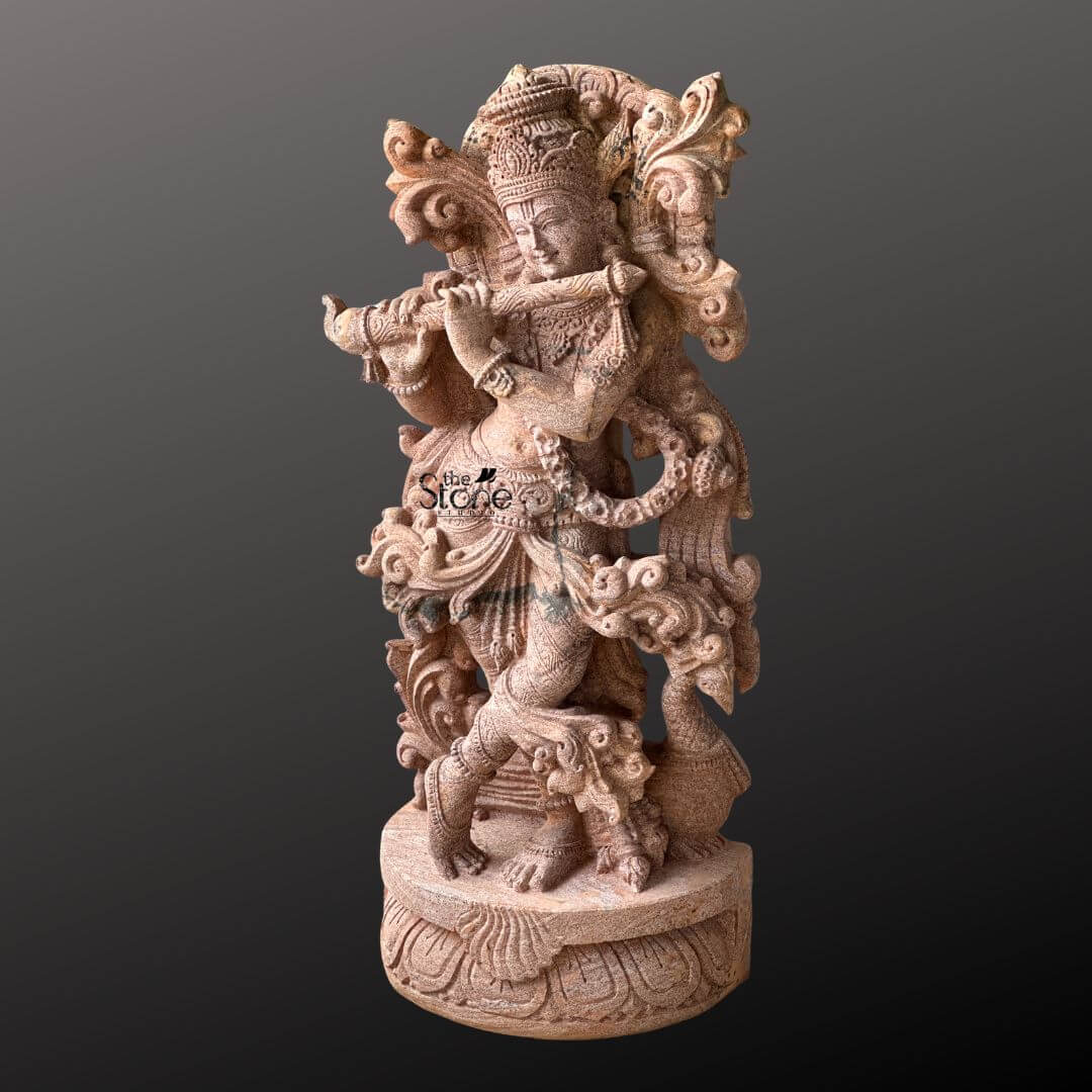 Standing Krishna Stone Statue with Flute 3.5ft 5 A magnificent 3.5-foot handcrafted Lord Krishna statue meticulously carved from sandstone stands elegantly against a deep contrasting background. The statue captures Krishna in his iconic Tribhanga pose with a graceful bend in his body as he plays his divine flute. His left leg is crossed delicately in front of his right creating a sense of dynamic movement and balance while his hands are positioned to hold the flute evoking the enchanting melodies for which he is celebrated. The sandstone sculpture is a testament to exceptional craftsmanship featuring a wealth of intricate details. Krishna is adorned with an elaborate crown likely depicting the revered peacock feather a symbol of beauty and divinity. His form is richly embellished with finely carved jewelry including multiple necklaces armlets a decorative waistband and anklets all contributing to his regal appearance. The flowing drapery of his dhoti and the intricately sculpted sashes appear to swirl around him adding to the statue's lifelike quality. Behind Krishna an ornate swirling motif possibly representing divine foliage or clouds frames his upper body enhancing his majestic presence. This 3.5-foot handcrafted sandstone Lord Krishna statue is an ideal focal point for an article highlighting artisanal stone sculptures. The warm earthy tones of the sandstone naturally enhance the intricate details and the spiritual aura of the deity. The skilled craftsmanship evident in every curve adornment and expressive element makes this statue a truly captivating and culturally significant piece embodying the charm and divine essence of Lord Krishna in a timeless and artistic form.