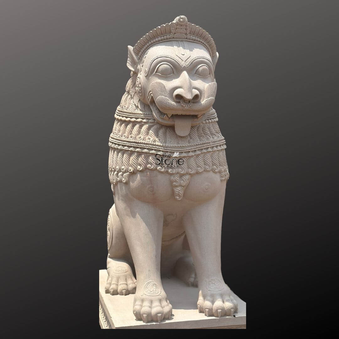 Traditional Stone Temple Lion Statue 7ft 5 A magnificent 7-foot Hindu Temple Lion Statue intricately carved from off-white sandstone is presented in a stately front-facing view against a dark plain background emphasizing its grandeur and commanding presence. The statue depicts a powerful lion in a seated alert posture its facial features stylized and adorned embodying strength guardianship and divine authority making it an iconic piece for temple entrances. The light natural hue of the sandstone allows the elaborate carvings to stand out vividly. The lion's face is central to the image featuring prominent watchful eyes a broad snout and an open mouth with a tongue extended conveying a sense of ferocity and protective power. Its mane is intricately carved with layers of textured patterns and decorative bands extending to its powerful chest. The body is robust and muscular with traditional swirling motifs and other embellishments visible on its legs and shoulders. Its large paws are firmly planted indicating stability and strength. The entire sculpture rests upon a robust multi-tiered base also adorned with intricate patterns providing a solid foundation and enhancing its imposing presence. This 7-foot off-white sandstone Hindu Temple Lion Statue is a profound representation of power protection and divine authority perfectly suited for the entrance of a temple or a significant spiritual site. The exceptional craftsmanship in sandstone not only makes it a visually striking piece but also imbues it with deep cultural and religious significance. This exquisitely detailed statue serves as a commanding sentinel radiating strength and an ancient spiritual presence embodying centuries of artistic tradition and architectural grandeur within Hindu temples.