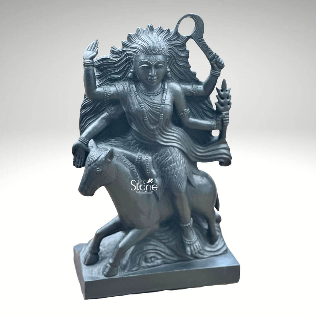 Black Stone Kaalratri Statue 15" 2 A powerful Kaalratri Devi statue carved from black stone is dynamically posed and presented against a clean white background. This fierce manifestation of the Divine Mother one of the Navadurga is depicted riding a horse symbolizing her swiftness and power in overcoming malevolence. Her hair appears unbound and flows dramatically emphasizing her formidable and untamed nature which aligns with her name meaning the night of blackness. The black stone statue of Kaalratri Devi is rich with symbolic and intricate details. The goddess is multi-armed with her hands wielding various weapons and ritual implements one hand prominently holds a saber or sword-like weapon aloft while another grasps a trident or a similar fiery object signifying her destructive power against evil. Her expression though intense conveys a sense of divine purpose and protective energy. She is adorned with sculpted jewelry including necklaces and bangles which stand out against her dark form. The horse she rides is captured mid-stride its legs seemingly galloping through stylized waves or clouds carved to enhance the sense of movement and raw power. The deep uniform black of the stone enhances the statue's dramatic and revered presence. This striking black stone Kaalratri Devi statue is an excellent visual for an article detailing such powerful deities. The choice of black stone perfectly embodies her dark transformative aspect while the intricate carving of her wild hair weapons and dynamic pose on the horse conveys her relentless energy. The statue is a compelling representation of Kaalratri's role in vanquishing fear ignorance and negativity making it a significant piece for devotees and art enthusiasts seeking to understand her divine might.