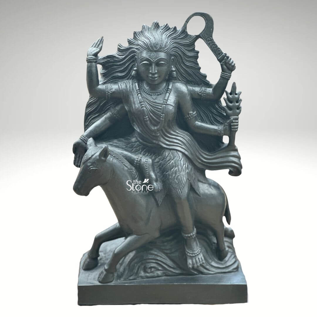 Black Stone Kaalratri Statue 15" 6 A powerful Kaalratri Murti carved from black stone is dynamically posed and presented against a clean white background. This fierce manifestation of the Divine Mother one of the Navadurga is depicted riding a horse symbolizing her swiftness and power in overcoming malevolence. Her hair appears unbound and flows dramatically upwards and outwards emphasizing her formidable and untamed nature which aligns with her name meaning the night of blackness. The black stone Kaalratri Murti is rich with symbolic and intricate details. The goddess is multi-armed with her hands wielding various weapons and ritual implements one hand prominently holds a saber or sword-like weapon aloft while another grasps a trident or a similar fiery object signifying her destructive power against evil. Her expression though intense conveys a sense of divine purpose and protective energy. She is adorned with sculpted jewelry including necklaces and bangles which stand out against her dark form. The horse she rides is captured mid-stride its legs seemingly galloping through stylized waves or clouds carved to enhance the sense of movement and raw power. The deep uniform black of the stone enhances the Murti's dramatic and revered presence. This striking black stone Kaalratri Murti is an excellent visual for an article detailing such powerful deities. The choice of black stone perfectly embodies her dark transformative aspect while the intricate carving of her wild hair weapons and dynamic pose on the horse conveys her relentless energy. The Murti is a compelling representation of Kaalratri's role in vanquishing fear ignorance and negativity making it a significant piece for devotees and art enthusiasts seeking to understand her divine might and incorporate her protective presence in their devotion.