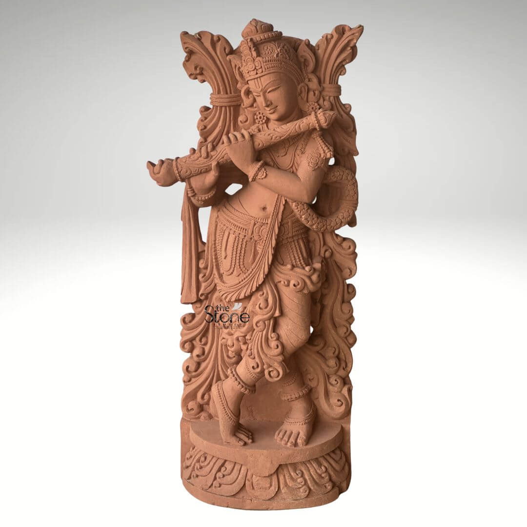 Lord Krishna Murti with Flute 3.5ft 2 A graceful 3.5-foot Krishna Bhagwan statue meticulously carved from sandstone depicted playing his flute making it an ideal spiritual addition for a home as prominently featured in an article about such sculptures. The entire statue rendered in the natural reddish-brown hue of sandstone exudes an earthy warm and timeless aesthetic. Lord Krishna is shown standing in his iconic Tribhanga pose with one leg crossed in front of the other an expression of divine playfulness and charm. He holds a flute to his lips with both hands appearing to play an enchanting melody. The carving details on Krishna's attire including his dhoti sash and intricate jewelry such as necklaces armlets and ankle bracelets are exceptionally refined. He wears an elaborate crown and a garland or Vanamala drapes diagonally across his body. The flowing drapery of his garments is skillfully sculpted adding a sense of movement and grace to the figure. Behind Krishna an intricately carved design possibly representing foliage or an artistic prabhavali further enhances the visual richness of the murti. The sculpture stands on a circular ornate pedestal also crafted from sandstone featuring traditional Indian architectural motifs and decorative patterns adding to its grandeur and stability. The texture of the sandstone is visible throughout providing depth and authenticity to the artwork. This 3.5-foot sandstone Krishna Bhagwan statue is a powerful representation of devotion and artistic mastery embodying the spiritual and aesthetic value discussed in the article making it an ideal centerpiece for spiritual veneration and artistic appreciation in a home.