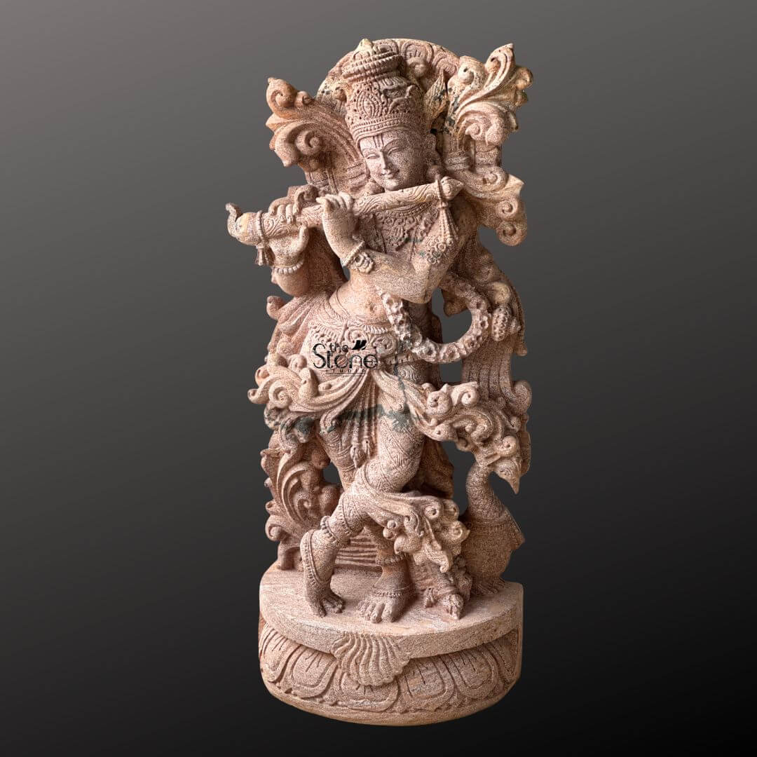 Standing Krishna Stone Statue with Flute 3.5ft 6 A stunning 3.5-foot Krishna Murti with a flute expertly carved from sandstone stands gracefully against a deep contrasting background. Lord Krishna is depicted in his iconic Tribhanga pose characterized by a triple bend in his body as he plays his bansuri. His left leg is crossed elegantly in front of his right conveying a sense of divine movement and enchanting rhythm while his hands are positioned precisely to hold the instrument symbolizing his melodious nature. The sandstone Murti is adorned with an array of intricate details that highlight its spiritual and artistic value. Krishna wears an elaborate crown which likely features the revered peacock feather a motif closely associated with his divine stories. His form is richly decorated with finely carved jewelry including multiple necklaces armlets a decorative waistband and anklets all meticulously rendered in the stone. The flowing drapery of his dhoti and the intricately sculpted sashes appear to swirl around him adding a dynamic and ethereal quality to the statue. Behind Krishna an ornate, swirling design possibly representing divine foliage or celestial clouds frames his upper body enhancing his majestic presence. This 3.5-foot sandstone Krishna Murti with a flute is an ideal visual for an article discussing such devotional sculptures. The warm, earthy tones of the sandstone naturally enhance the intricate carvings and the spiritual aura of the deity. The skilled craftsmanship evident in every curve adornment and expressive element makes this Murti a truly captivating and culturally significant piece embodying the charm and divine essence of Lord Krishna in a timeless and artistic form perfect for worship or decorative display.