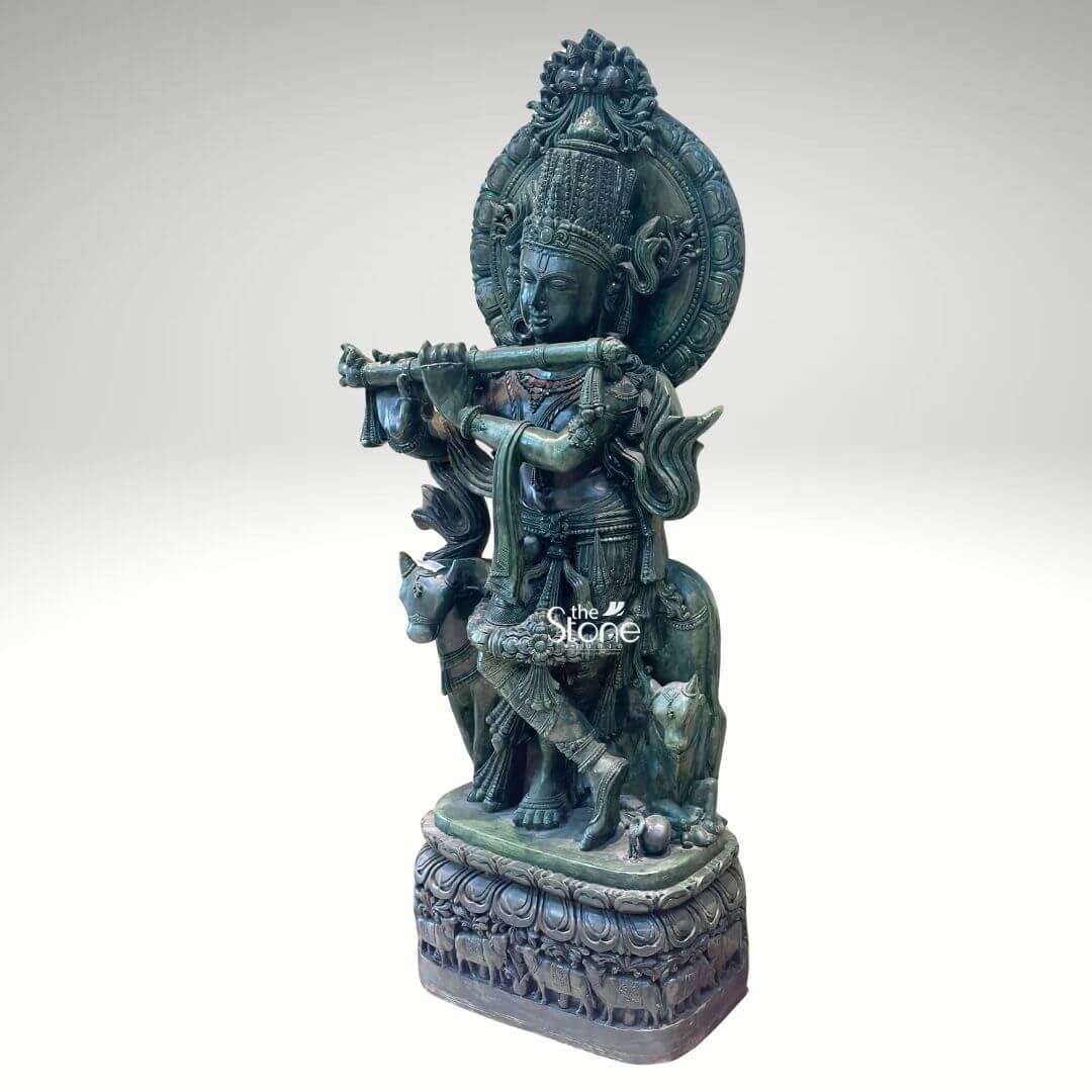 Green Stone Krishna with Cow Statue 4ft 5 A magnificent Krishna with Cow and Calf Statue meticulously carved from greenstone stands prominently against a clean white background showcasing exquisite detail and artistry. Lord Krishna is depicted in his iconic Tribhanga pose gracefully playing his flute his body angled with a serene expression. Beside him a cow and a calf are intricately carved reflecting his identity as a divine cowherd an essential aspect of the Krishna with Cow and Calf theme. The greenstone material gives the entire sculpture a distinctive earthy and revered appearance. The greenstone Krishna statue is rich with traditional ornamentation. Krishna wears an elaborate crown likely adorned with a peacock feather a symbol strongly associated with him. His form is embellished with finely carved jewelry including necklaces armlets waistbands and anklets. The flowing drapery of his dhoti and sashes adds to the dynamic quality of the pose. Behind Krishna a circular aureole or halo frames his head often symbolizing divinity and a larger ornate arch rises above featuring intricate patterns. The cow and calf are rendered with gentle expressions symbolizing prosperity devotion and the tender bond between mother and offspring and they are surrounded by carved foliage and other natural elements. This Green Stone Krishna with Cow and Calf statue is an ideal visual for an article detailing such divine sculptures. The statue rests on a multi-tiered intricately carved base which features a band of smaller animal figures possibly more cows further enhancing the pastoral theme. The harmonious composition of Krishna the cow and calf and the detailed base in greenstone creates a powerful and spiritually uplifting piece embodying devotion divine love and the sacred bond between Krishna animals and nature perfect for a temple or a home seeking a touch of spiritual grace.