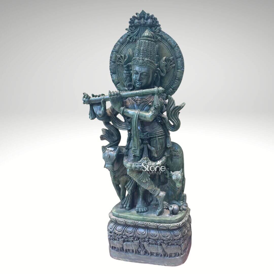 Green Stone Krishna with Cow Statue 4ft 4 A magnificent Lord Krishna Flute Statue with Cow meticulously carved from greenstone stands prominently against a clean white background showcasing exquisite detail and artistry. Lord Krishna is depicted in his iconic Tribhanga pose gracefully playing his flute his body angled with a serene expression. Beside him a cow and a calf are intricately carved reflecting his identity as a divine cowherd an essential aspect of the Krishna Flute Statue with Cow theme. The greenstone material gives the entire sculpture a distinctive earthy and revered appearance. The greenstone Lord Krishna statue is rich with traditional ornamentation. Krishna wears an elaborate crown likely adorned with a peacock feather a symbol strongly associated with him. His form is embellished with finely carved jewelry including necklaces armlets waistbands and anklets. The flowing drapery of his dhoti and sashes adds to the dynamic quality of the pose. Behind Krishna a circular aureole or halo frames his head often symbolizing divinity and a larger ornate arch rises above featuring intricate patterns. The cow and calf are rendered with gentle expressions symbolizing prosperity devotion and the tender bond between mother and offspring and they are surrounded by carved foliage and other natural elements. This Green Stone Lord Krishna Flute Statue with Cow is an ideal visual for an article detailing such divine sculptures. The statue rests on a multi-tiered intricately carved base which features a band of smaller animal figures possibly more cows further enhancing the pastoral theme. The harmonious composition of Krishna the cow and calf and the detailed base in greenstone creates a powerful and spiritually uplifting piece embodying devotion divine love and the sacred bond between Krishna animals and nature perfect for a temple or a home seeking a touch of spiritual grace.