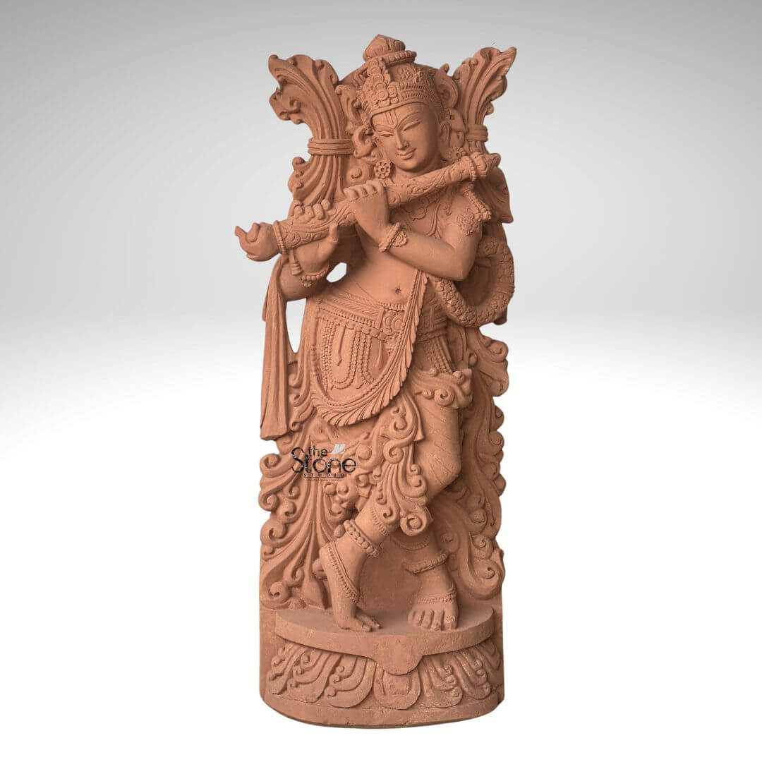 Lord Krishna Murti with Flute 3.5ft 1 A graceful 3.5-foot Lord Krishna Murti meticulously carved from sandstone depicted playing his flute as prominently featured in an article about such sculptures. The entire statue rendered in the natural reddish-brown hue of sandstone exudes an earthy warm and timeless aesthetic. Lord Krishna is shown standing in his iconic Tribhanga pose with one leg crossed in front of the other an expression of divine playfulness and charm. He holds a flute to his lips with both hands appearing to play a enchanting melody. The carving details on Krishna's attire including his dhoti sash and intricate jewelry such as necklaces armlets and ankle bracelets are exceptionally refined. He wears an elaborate crown and a garland or Vanamala drapes diagonally across his body. The flowing drapery of his garments is skillfully sculpted adding a sense of movement and grace to the figure. Behind Krishna an intricately carved design possibly representing foliage or an artistic prabhavali further enhances the visual richness of the murti. The sculpture stands on a circular ornate pedestal also crafted from sandstone featuring traditional Indian architectural motifs and decorative patterns adding to its grandeur and stability. The texture of the sandstone is visible throughout providing depth and authenticity to the artwork. This 3.5-foot sandstone Krishna murti is a powerful representation of devotion and artistic mastery, embodying the spiritual and aesthetic value discussed in the article making it an ideal centerpiece for spiritual veneration and artistic appreciation in a home or garden.