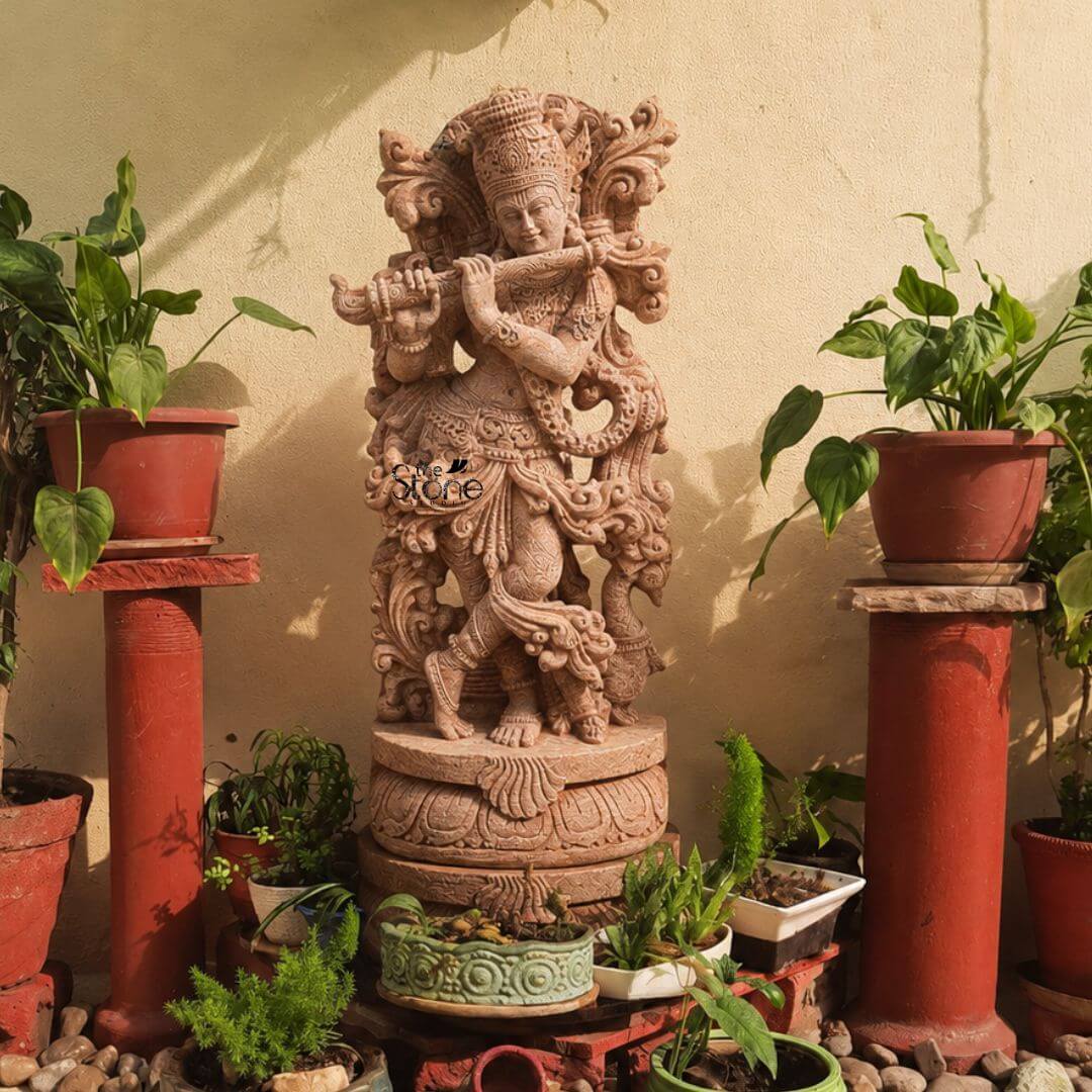 Standing Krishna Stone Statue with Flute 3.5ft 3 A striking 3.5-foot Lord Krishna statue with a peacock carved from sandstone stands as the centerpiece of a vibrant outdoor setting likely a garden or patio against a warm light-colored wall. Lord Krishna is depicted in his iconic Tribhanga pose gracefully playing his flute with his left leg crossed over his right conveying a sense of divine melody and enchanting movement. A distinct peacock figure is integrated into the intricate carvings at the base near Krishna's feet connecting directly to the article's theme. The sandstone sculpture is rich with elaborate details that highlight its artistic and spiritual significance. Krishna wears an ornate crown which often features a peacock feather a quintessential symbol of the deity. His form is adorned with finely carved jewelry including multiple necklaces armlets a decorative waistband and anklets all meticulously rendered in the warm-toned stone. The flowing drapery of his dhoti and the intricately sculpted sashes appear to swirl around him adding a dynamic quality. The presence of the peacock subtly yet clearly carved reinforces Krishna's deep connection to this sacred bird especially in the elaborate back arch that frames his upper body. This 3.5-foot sandstone Lord Krishna statue with a peacock is an excellent visual for an article detailing such specialized sculptures. The natural earthy tones of the sandstone blend harmoniously with the surrounding potted plants and reddish-brown pedestals creating an inviting and spiritual atmosphere. The skilled craftsmanship particularly the integrated peacock element and Krishna's serene flute-playing posture makes this statue a captivating and culturally significant piece embodying the charm and divine essence of Lord Krishna in a timeless and artistic form perfect for any garden or home.