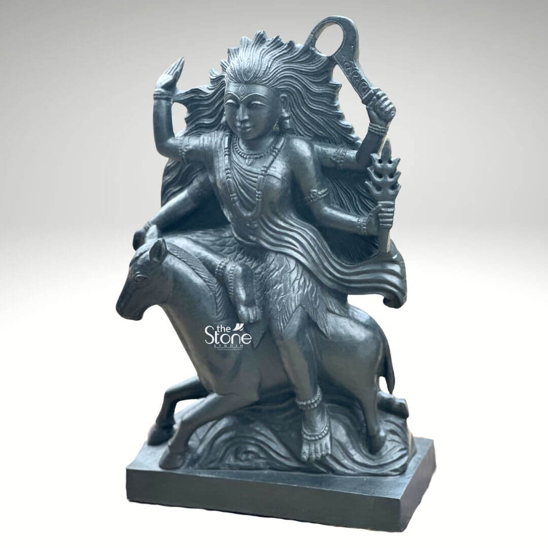 Black Stone Kaalratri Statue 15" 7 A powerful Maa Kaalratri idol carved from black stone is dynamically posed and presented against a clean white background. This fierce manifestation of the Divine Mother one of the Navadurga is depicted riding a horse symbolizing her swiftness and power in overcoming malevolence. Her hair appears unbound and flows dramatically upwards and outwards emphasizing her formidable and untamed nature which aligns with her name meaning the night of blackness. The black stone Maa Kaalratri idol is rich with symbolic and intricate details. The goddess is multi-armed with her hands wielding various weapons and ritual implements one hand prominently holds a saber or sword-like weapon aloft while another grasps a trident or a similar fiery object signifying her destructive power against evil. Her expression though intense conveys a sense of divine purpose and protective energy. She is adorned with sculpted jewelry including necklaces and bangles which stand out against her dark form. The horse she rides is captured mid-stride its legs seemingly galloping through stylized waves or clouds carved to enhance the sense of movement and raw power. The deep uniform black of the stone enhances the idol's dramatic and revered presence. This striking black stone Maa Kaalratri idol is an excellent visual for an article detailing such powerful deities. The choice of black stone perfectly embodies her dark transformative aspect while the intricate carving of her wild hair weapons and dynamic pose on the horse conveys her relentless energy. The idol is a compelling representation of Maa Kaalratri's role in vanquishing fear ignorance and negativity making it a significant piece for devotees and art enthusiasts seeking to understand her divine might and incorporate her protective presence in their devotion.