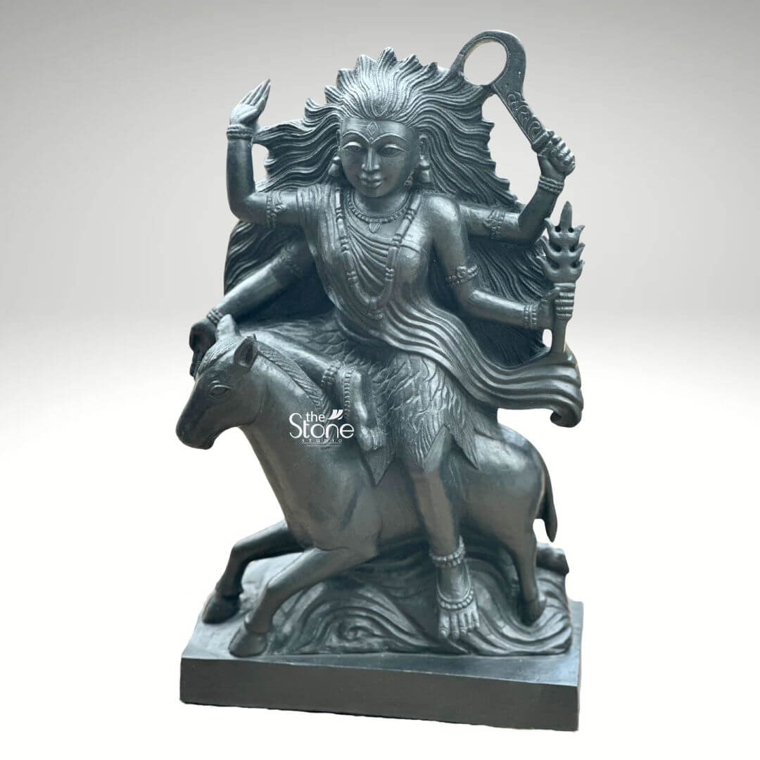 Black Stone Kaalratri Statue 15" 8 A powerful Maa Kaalratri Murti carved from black stone is dynamically posed and presented against a clean white background. This fierce manifestation of the Divine Mother one of the Navadurga is depicted riding a horse symbolizing her swiftness and power in overcoming malevolence. Her hair appears unbound and flows dramatically upwards and outwards emphasizing her formidable and untamed nature which aligns with her name meaning the night of blackness. The black stone Maa Kaalratri Murti is rich with symbolic and intricate details. The goddess is multi-armed with her hands wielding various weapons and ritual implements one hand prominently holds a saber or sword-like weapon aloft while another grasps a trident or a similar fiery object signifying her destructive power against evil. Her expression though intense conveys a sense of divine purpose and protective energy. She is adorned with sculpted jewelry including necklaces and bangles which stand out against her dark form. The horse she rides is captured mid-stride its legs seemingly galloping through stylized waves or clouds carved to enhance the sense of movement and raw power. The deep uniform black of the stone enhances the Murti's dramatic and revered presence. This striking black stone Maa Kaalratri Murti is an excellent visual for an article detailing such powerful deities. The choice of black stone perfectly embodies her dark transformative aspect while the intricate carving of her wild hair weapons and dynamic pose on the horse conveys her relentless energy. The Murti is a compelling representation of Maa Kaalratri's role in vanquishing fear ignorance and negativity making it a significant piece for devotees and art enthusiasts seeking to understand her divine might and incorporate her protective presence in their devotion.