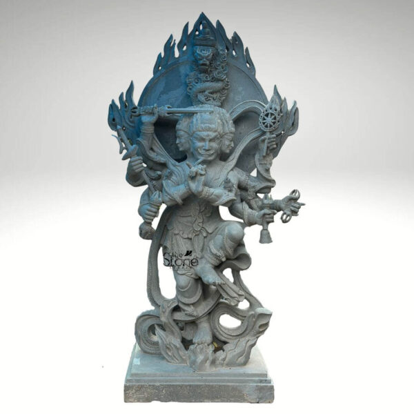 A powerful and intricately carved Mahakala Dharmapala statue rendered in a dark grey stone stands dynamically against a clean white background. This multi-headed and multi-armed deity is depicted in a fierce wrathful form characteristic of a Dharmapala a protector of the Dharma in Vajrayana Buddhism. The central figure has multiple faces possibly three or four each with intense expressions signifying his all-seeing nature and unwavering resolve to overcome obstacles. The statue is rich with symbolic details. Mahakala holds various ritual implements in his many hands such as a kartika, a kapala a trident and other weapons all representing his power to cut through delusions and consume negativities. Flames and intricate patterns rise dramatically behind him forming a fiery aureole that emphasizes his fierce protective energy. A small subtle dragon or mythical creature is carved into the top of this fiery arch adding to the mythical grandeur. The deity's posture is dynamic with bent knees suggesting readiness for action and he stands upon a base that appears to include stylized forms of defeated foes or obstacles symbolizing his triumph over evil. This striking grey stone Mahakala Dharmapala statue is an exceptional example for an article exploring such protector deities. The dark stone enhances the intimidating yet protective presence of Mahakala making his wrathful form profoundly impactful. The intricate carvings of his faces hands implements and the fiery backdrop all contribute to a powerful representation of a Dharmapala embodying strength protection and the fierce eradication of ignorance and defilements.