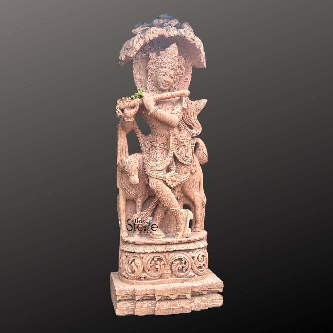 Large Krishna Stone Sculpture with Cow 6ft 5 A captivating 6-foot outdoor Krishna statue meticulously carved from natural brown sandstone presented against a dark minimalist background as detailed in an article about such sculptures. Lord Krishna is depicted in his iconic Tribhanga posture gracefully holding a flute to his lips emanating divine music. The natural reddish-brown hue and coarse texture of the sandstone lend a timeless and earthy aesthetic to the artwork highlighting the intricate details of the carving. Krishna is adorned with an elaborate crown and traditional jewelry including necklaces armlets and ankle bracelets all skillfully chiseled from the stone. The carving details extend to Krishna's flowing dhoti and sash which show a remarkable sense of movement and drapery. His serene facial expression with a gentle smile and slightly tilted head captures his divine charm and evokes a sense of peace. Notably a small green leaf or flower is placed on the flute adding a subtle touch of realism and a pop of color to the otherwise monochromatic sculpture. Standing gently beside Krishna to his left is a cow a sacred companion symbolizing purity and abundance. The cow's form is also intricately carved with a calm demeanor further reinforcing Krishna's role as a protector of cows and a benevolent deity. The entire sculpture rests on a robust and intricately carved multi-tiered pedestal also crafted from sandstone featuring traditional Indian architectural motifs and decorative patterns that enhance its grandeur and stability. Above Krishna an ornate canopy or arch resembling lush foliage or an artistic temple arch provides a dignified frame. This 6-foot outdoor Krishna statue is a powerful representation of devotion and artistry perfectly suited to withstand outdoor elements while enhancing the beauty and tranquility of any garden or courtyard embodying the spiritual and aesthetic value discussed in the article.