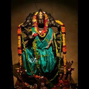 A powerful 5 Feet Blackstone Panchamukhi Hanuman Statue adorned with vibrant offerings stands majestically in what appears to be a dimly lit shrine or temple possibly in Srikakulam as suggested by its article context. This Panchamukhi Hanuman Stone Statue is intricately carved from dark blackstone depicting Lord Hanuman with his iconic five faces each representing a different aspect and power. The central face is Hanuman's flanked by four other divine faces all emanating strength and divine presence. The statue's imposing height and dark material make it a commanding figure central to devotion. Lord Hanuman is richly draped in a lustrous teal-blue silk dhoti and shawl adorned with a vibrant array of fresh flower garlands. These garlands primarily yellow and orange marigolds interspersed with green beads or leaves, are elaborately hung around his neck and extend down his multiple arms. Hanuman is depicted with numerous arms characteristic of Panchamukhi iconography each holding a divine weapon or gesture. One hand is raised in a gesture of blessing while others grasp various attributes. The smooth polished blackstone contrasts beautifully with the colorful fabric and fresh flowers creating a visually striking devotional image. At the base of the statue offerings of fresh flowers including red hibiscus and white blossoms are scattered indicating active worship. Two traditional brass oil lamps illuminate the statue from either side casting a warm glow that accentuates the details of the blackstone and the vibrant colors of the offerings. The dark simple background ensures that the "5 Feet Blackstone Panchamukhi Hanuman Statue remains the absolute focal point. This detailed description effectively connects the visual elements of the blackstone sculpture with its spiritual significance and aesthetic qualities, making it an ideal representation for an article about a Panchamukhi Hanuman Stone Statue in Srikakulam emphasizing its sacred and powerful presence.