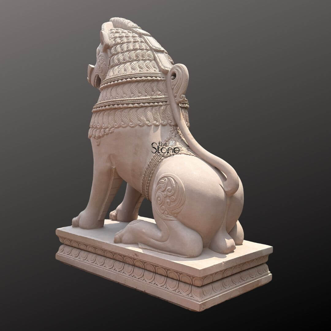 Traditional Stone Temple Lion Statue 7ft 6 A magnificent 7-foot Sacred Stone Lion Guardian Statue intricately carved from off-white sandstone is presented from a rear-right slightly elevated perspective against a dark plain background. This viewpoint emphasizes the lion's powerful physique and the intricate decorative carvings highlighting its role as a majestic and sacred guardian. The light natural hue of the sandstone allows the elaborate details to stand out vividly showcasing the exceptional craftsmanship involved in creating this traditional piece. The lion is depicted in a seated alert posture with its powerful hindquarters and robust legs prominently displayed conveying a sense of grounded strength. Its tail curls elegantly along its back terminating in an ornamental flourish a characteristic of traditional stone art. The mane is intricately carved with layers of textured patterns and decorative bands extending around its neck and shoulders. Swirling motifs and other traditional embellishments are visible on its flank and haunches adding depth and cultural richness to the sculpture. The entire sculpture rests upon a robust multi-tiered base also adorned with intricate patterns providing a solid foundation and enhancing its imposing presence as a guardian. This 7-foot off-white sandstone Sacred Stone Lion Guardian Statue is a profound representation of power, protection and divine authority perfectly suited for the entrance of a temple a sacred shrine or a significant architectural site. The exceptional craftsmanship in sandstone not only makes it a visually striking piece but also imbues it with deep cultural and religious significance. This exquisitely detailed statue serves as a commanding sentinel radiating strength and an ancient spiritual presence embodying centuries of artistic tradition and the sacred role of a guardian.