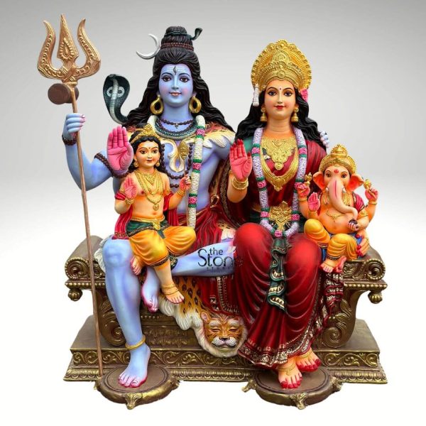 A magnificent 5.5 feet Shiv Parivar Fibre Statue vibrant with color and intricate details is presented against a clean light background showcasing the divine family in all their splendor. This Shiv Parivar Fibre Statue depicts Lord Shiva Goddess Parvati and their sons Ganesha and Kartikeya seated together on an ornate throne symbolizing harmony prosperity and cosmic balance. The fiber material allows for vivid colors and fine craftsmanship giving the statue a lifelike and devotional appeal. Lord Shiva with his iconic blue skin sits on the left his right hand raised in a gesture of blessing. His dark hair is styled in a jatamukuta adorned with a crescent moon and a cobra around his neck. He wears a tiger skin dhoti with the tiger's head prominently carved at the front of the throne beneath him representing his mastery over desire. Kartikeya with golden skin sits on Shiva's lap, also blessing with his right hand. Goddess Parvati with radiant golden skin sits elegantly on the right draped in a rich red sari with gold borders and adorned with elaborate gold jewelry and garlands. Her right hand is also raised in a blessing gesture. Little Ganesha with his elephant head and golden skin sits on Parvati's lap holding a modak. The entire divine family is seated on a grand golden-bronze throne intricately carved with traditional patterns and supported by ornate legs. A prominent golden trident stands tall beside Lord Shiva symbolizing his power. The colorful details on their attire jewelry and features bring the deities to life making this 5.5 feet Shiva Parivar Fibre Statue a captivating center for worship. This detailed description effectively connects the visual elements of the fiber sculpture with its spiritual significance and aesthetic qualities making it an ideal representation for an article about a Shiv Parivar Fibre Statue.