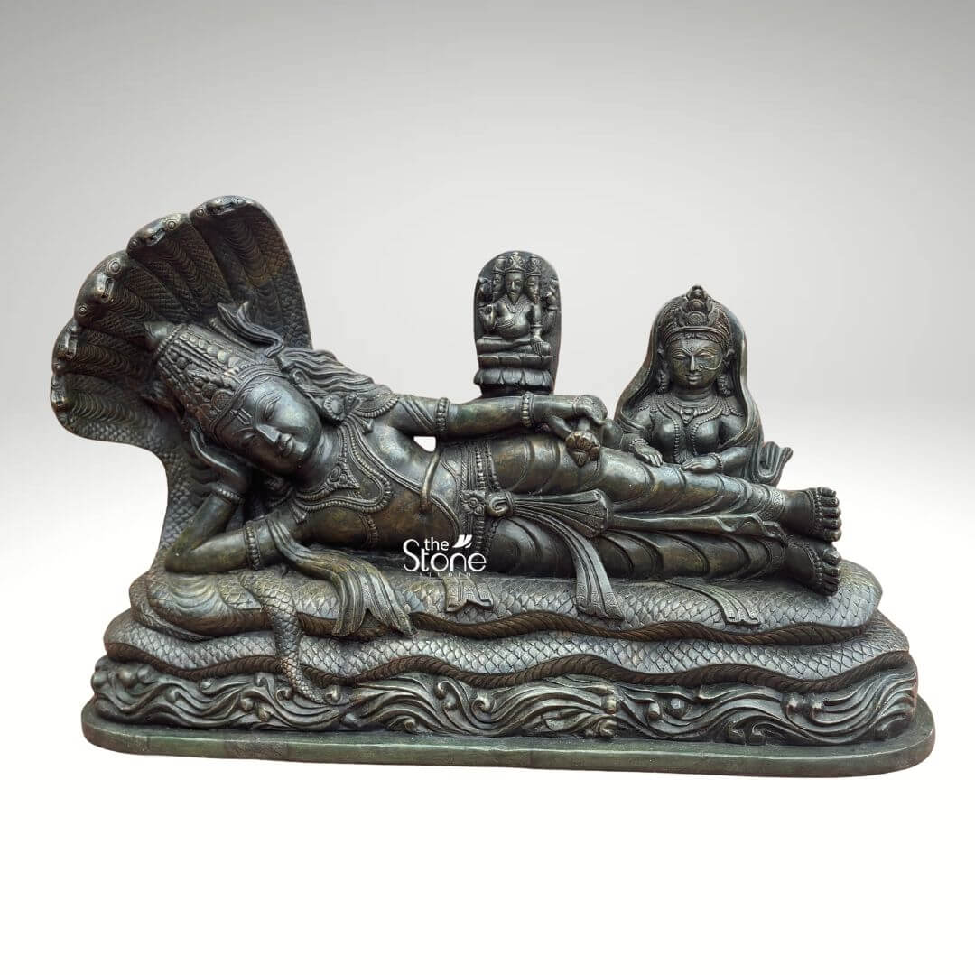 Ananta Shayana Vishnu Statue 20" 11 A magnificent green stone sculpture of Lord Vishnu in his iconic sleeping posture is presented making it an ideal piece for a puja room. The statue captures Vishnu reclining on the cosmic serpent Sheshnag symbolizing the universe's cyclical nature of dissolution and creation. The deep rich green hue of the stone possibly a dark serpentine or steatite provides a majestic and ancient aesthetic highlighting the intricate details of the figures and the serene spiritual narrative creating a profound focal point for worship. Lord Vishnu is meticulously carved in a state of serene cosmic slumber his head gently supported by his right arm with an expression of profound peace and detachment. He is lavishly adorned with traditional Hindu ornaments including an elaborate crown multiple necklaces intricate armlets and a gracefully draped dhoti all carved with exceptional precision. The multi-headed Sheshnag coils beneath him its numerous hoods fanning out to form a grand protective canopy over Vishnu's head with its scales and undulating body intricately rendered to suggest movement and power. From Vishnu's navel a delicate lotus emerges bearing a miniature figure of Brahma the creator god. To Vishnu's right seated attentively is Goddess Lakshmi his divine consort her form equally adorned and sculpted with reverence attending to his feet. This green stone Sleeping Vishnu sculpture is a powerful and sacred representation of preservation cosmic order and the continuous cycle of time perfectly suited for a puja room. The exceptional detail and the choice of green stone often associated with spiritual balance and renewal significantly enhance its profound symbolism. This exquisitely crafted statue is an impressive and deeply meaningful artifact inviting contemplation and reverence for the divine cosmic dance and enriching any sacred space with its deep cultural and religious resonance.