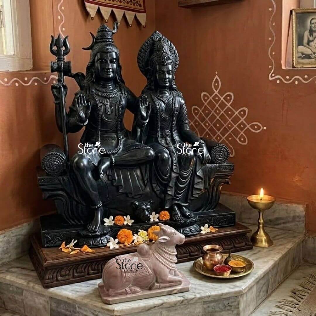 Stone Nandi Statue for Home Temple 8" 3 A beautifully arranged home mandir features a prominent black stone statue of Lord Shiva and Goddess Parvati seated together with an 8-inch pink stone Nandi statue positioned reverently in front. The primary focus of the image is the smaller detailed pink stone Nandi which is situated on a lower step symbolizing its role as the divine vehicle and gatekeeper to Lord Shiva. The warm earthy tones of the background wall adorned with traditional white rangoli patterns create an inviting and sacred atmosphere. The 8-inch Nandi statue carved from natural pink stone is depicted in a peaceful seated posture its head gently turned towards the larger deities. The soft pink hue of the stone contrasts gently with the darker elements of the main idols and the wooden base drawing attention to its delicate craftsmanship. Flowers scattered around the base of the larger statue and near the Nandi add to the devotional setting along with a lit oil lamp on a brass stand casting a soft glow on the offerings. This image beautifully illustrates the ideal placement of a small Nandi statue in a home mandir emphasizing its significance in Hindu worship. The 8-inch pink stone Nandi placed before the divine couple represents devotion purity and strength and is an essential element for a complete Shiva puja. The thoughtful arrangement of the deities offerings and the serene Nandi statue creates a powerful visual narrative of faith and reverence within a personal sacred space.