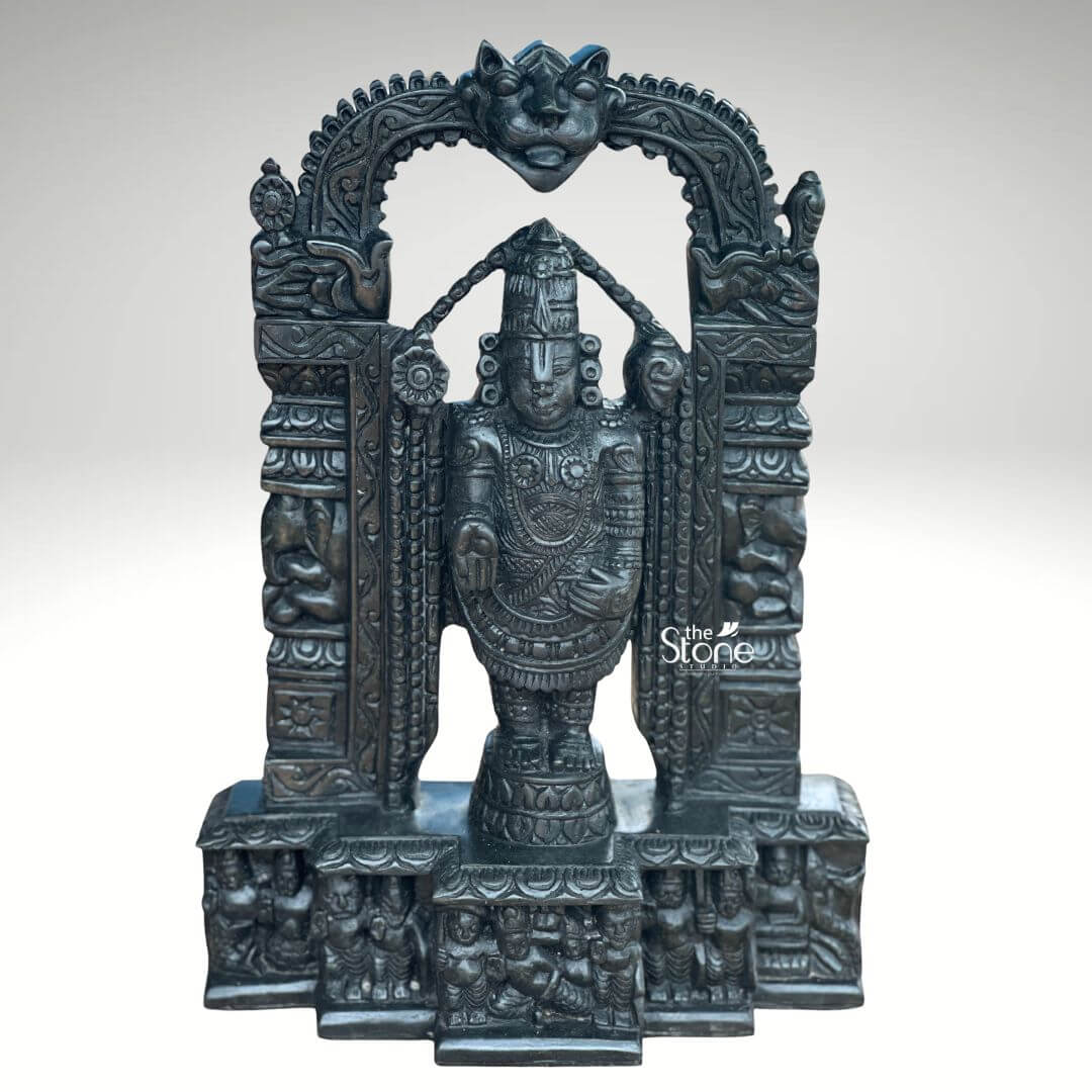 Tirupati Balaji Statue in Black Stone 18" 1 An exquisite 18-inch Tirupati Balaji statue meticulously carved from black stone stands majestically within an elaborate archway presented against a plain light background. This stunning black stone Balaji statue captures the revered deity Lord Venkateswara in his iconic standing pose exuding an aura of divine grace and power. The dark polished surface of the stone provides a dramatic contrast enhancing the intricate details of the sculpture and its ornate architectural frame. Lord Balaji is depicted with his characteristic features including the prominent Urdhva Pundra on his forehead elaborate crown and various traditional ornaments such as multiple necklace armlets and a sacred thread. His right hand is raised in the Abhaya Mudra offering blessings and reassurance while his left hand rests on his thigh symbolizing protection. He stands on a lotus pedestal which is integrated into a multi-tiered base adorned with smaller figures and decorative carvings including devotees and mythological scenes all contributing to the grandeur of the piece. The archway above him is intricately detailed featuring divine figures floral motifs and a Kirtimukha at the apex. This 18-inch black stone Tirupati Balaji statue is a profound representation of Lord Venkateswara the preserver of the universe and is a perfect centerpiece for a home temple or a significant spiritual collection. The exceptional craftsmanship in black stone not only makes it a visually striking piece but also embodies deep cultural and religious significance offering a powerful focal point for devotion and prayer. The rich detailing of the deity and his surrounding archway reflects centuries of tradition making it a truly remarkable and revered artifact.
