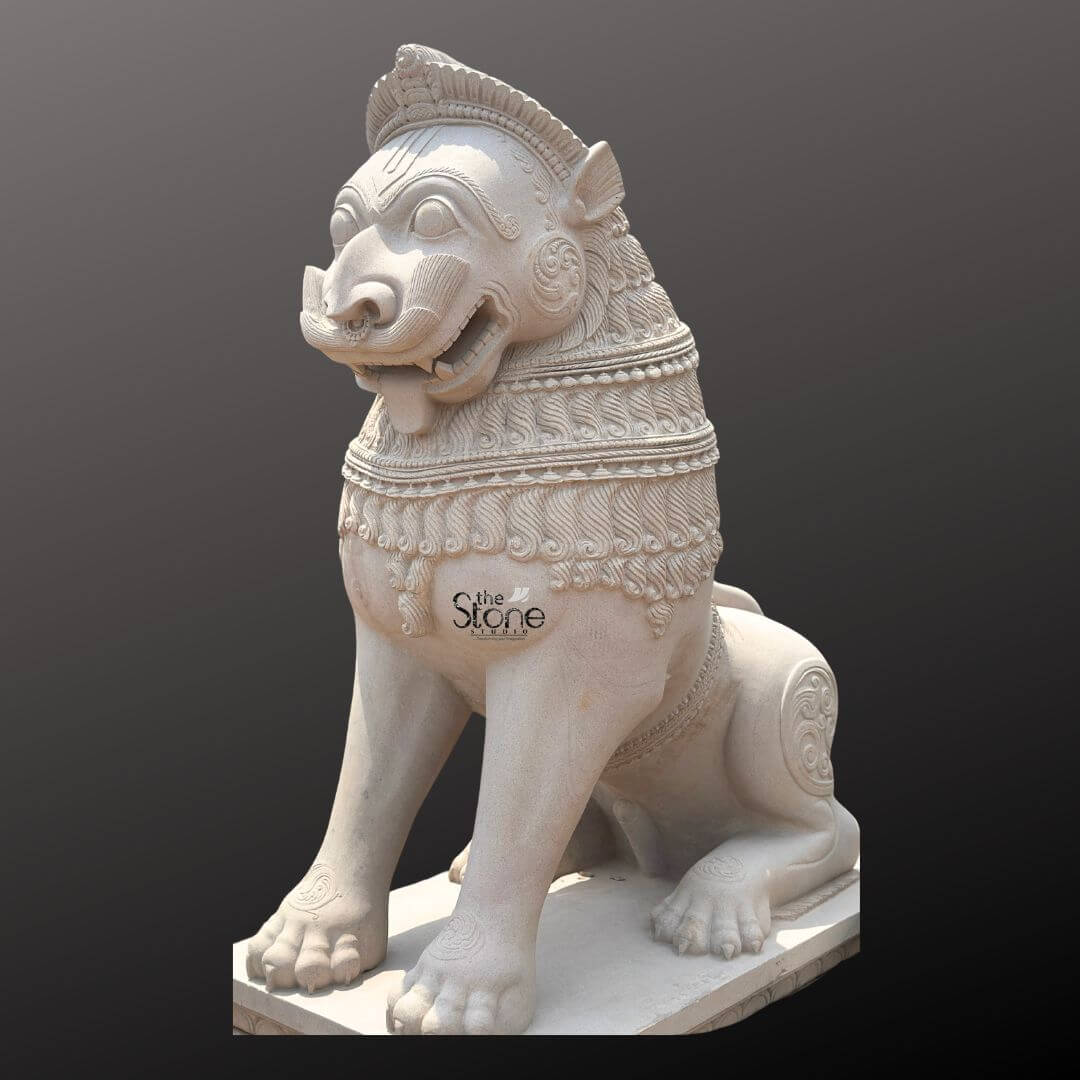 Traditional Stone Temple Lion Statue 7ft 11 A magnificent 7-foot Traditional Simha Stone Sculpture intricately carved from off-white sandstone is presented in a stately side profile against a dark plain background emphasizing its grandeur and commanding presence. The statue depicts a powerful in a seated alert posture its facial features stylized and adorned, embodying strength, guardianship and regal authority making it an iconic piece of traditional art. The light, natural hue of the sandstone allows the elaborate carvings to stand out vividly. The lion's features are highly stylized and ornamental, typical of traditional stone carving. Its mane is intricately carved with layers of textured patterns, resembling scales or braided hair, and its powerful neck is adorned with decorative bands. The lion's face, seen in profile, features prominent eyes, a strong snout, and an open mouth, conveying a sense of watchful guardianship and a roaring presence. Its muscular body is embellished with swirling motifs and decorative elements on its shoulders and hindquarters. The tail curls elegantly along its back, terminating in an ornamental flourish. The entire sculpture rests upon a robust, multi-tiered base (partially visible), providing a solid foundation and enhancing its imposing presence. This 7-foot off-white sandstone Traditional Simha Stone Sculpture is a profound representation of power, protection, and majesty, rooted in centuries of artistic and cultural heritage. The exceptional craftsmanship in sandstone not only makes it a visually striking piece but also imbues it with deep cultural and artistic significance. This exquisitely detailed statue serves as a commanding figure, radiating strength and an ancient presence, embodying the rich traditions of stone sculpture and the revered image of the Simha in various architectural and spiritual contexts.