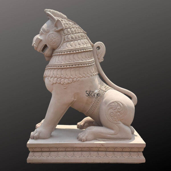 A magnificent 7-foot traditional stone temple lion statue carved from off-white sandstone is presented in a majestic side profile against a dark plain background emphasizing its grandeur and intricate details. The statue depicts a powerful lion in a seated alert posture embodying strength guardianship and regal authority making it an iconic piece for temple entrances or grand architectural settings. The light natural hue of the sandstone allows the elaborate carvings to stand out vividly. The lion's features are highly stylized and ornamental typical of traditional temple art. Its mane is intricately carved with layers of textured patterns resembling scales or braided hair and its powerful neck is adorned with decorative bands. The lion's face seen in profile features prominent eyes a strong snout and an open mouth conveying a sense of watchful guardianship. Its muscular body is embellished with swirling motifs and decorative elements on its shoulders and hindquarters. The tail curls elegantly along its back terminating in an ornamental flourish. The entire sculpture rests upon a robust multi-tiered base also adorned with intricate patterns providing a solid foundation and enhancing its imposing presence. This 7-foot off-white sandstone Traditional Stone Temple Lion Statue is a profound representation of power protection and divine authority perfectly suited for the entrance of a temple or a significant architectural site. The exceptional craftsmanship in sandstone not only makes it a visually striking piece but also imbues it with deep cultural and religious significance. This exquisitely detailed statue serves as a commanding sentinel radiating strength and an ancient spiritual presence embodying centuries of artistic tradition and architectural grandeur.
