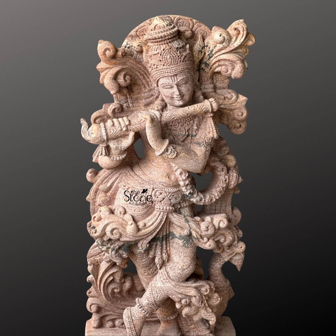 Standing Krishna Stone Statue with Flute 3.5ft 10 A magnificent 3.5-foot Venugopal Krishna stone idol meticulously carved from sandstone stands elegantly against a deep contrasting background. Lord Krishna is depicted in his iconic Tribhanga pose characterized by a triple bend in his body as he plays his divine bansuri which identifies him as Venugopal the cowherd who plays the flute. His left leg is crossed delicately in front of his right creating a sense of dynamic movement and artistic balance while his hands are positioned to hold the flute evoking the enchanting melodies for which he is celebrated. The sandstone idol is a testament to exceptional craftsmanship featuring a wealth of intricate details that highlight its artistic and spiritual significance. Krishna is adorned with an elaborate crown exquisitely carved with patterns and possibly featuring the revered peacock feather a quintessential symbol of his divine persona. His form is richly embellished with finely carved jewelry including multiple necklaces armlets a decorative waistband and anklets all rendered with precision in the warm-toned stone. The flowing drapery of his dhoti and the intricately sculpted sashes appear to swirl around him adding to the statue's lifelike quality. Behind Krishna an ornate, swirling motif possibly representing divine foliage or celestial clouds frames his upper body enhancing his majestic presence. This 3.5-foot sandstone Venugopal Krishna idol is an ideal focal point for an article specifically highlighting this beloved form of Krishna. The warm earthy tones of the sandstone naturally enhance the intricate carvings and the spiritual aura of the deity. The skilled craftsmanship evident in every curve adornment and expressive element makes this idol a truly captivating and culturally significant piece embodying the charm and divine essence of Lord Krishna as the flute-playing cowherd in a timeless and artistic form perfect for worship or decorative display.