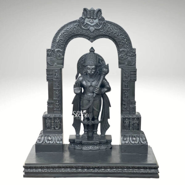 A commanding Black Stone Hanuman Statue with an Arch meticulously carved from dark black stone stands prominently against a clean white background creating a powerful visual impact. Lord Hanuman is depicted in a standing posture radiating strength and devotion. He is adorned with an elaborate crown intricate jewelry and flowing garments all finely sculpted from the lustrous black stone. In his left hand he firmly grasps his gada a symbol of his immense power and valor while his right hand is raised in a gesture of reassurance or blessing. The statue is dramatically framed by a beautifully carved arch that features intricate traditional patterns and motifs characteristic of temple architecture. The arch is supported by two ornate pillar each also adorned with detailed carvings further enhancing the grandeur and spiritual significance of the entire piece. The deep black color of the stone emphasizes the intricate details of Hanuman's musculature his serene yet determined expression and the delicate patterns of his adornments. The entire sculpture including the arch and pillars rests on a multi-tiered base also carved from black stone which provides stability and adds to its stately presence. This impressive 3-foot Black Stone Hanuman statue with its integrated arch is an exquisite example of religious artistry making it an ideal centerpiece for a home temple a place of worship or as a significant cultural statement piece. Its detailed craftsmanship and powerful depiction of Lord Hanuman align perfectly with an article focusing on such a statue symbolizing strength loyalty and devotion.