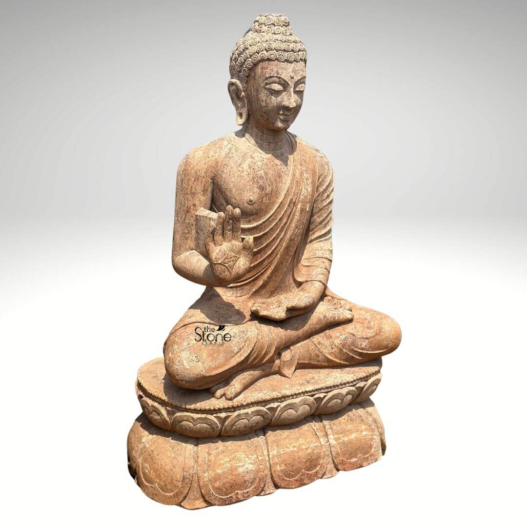 Sandstone Buddha Statue in Abhaya Mudra 3ft 4 A magnificent 3-foot Sandstone Buddha statue prominently featured on a beautifully carved lotus pedestal stands against a clean light grey background radiating an aura of ancient wisdom and serenity. The statue carved from a warm reddish-brown sandstone depicts Buddha in a meditative seated posture specifically the full lotus position symbolizing deep concentration and spiritual enlightenment. His right hand is raised to shoulder height with the palm facing outward fingers extended upwards forming the Abhaya Mudra the gesture of fearlessness and blessing. His left hand rests gently in his lap palm upwards signifying contemplation and receptivity. The natural earthy hue and weathered texture of the sandstone give the sculpture an authentic timeless feel highlighting its intricate details. The Buddha's facial features are exquisitely carved radiating profound peace and wisdom. His eyes are gently closed or cast downwards in contemplation and a subtle serene smile graces his lips. His head is adorned with tightly coiled hair culminating in the ushnisha the cranial bump symbolizing his supreme spiritual knowledge and enlightenment. The flowing drapery of his robes is sculpted with soft elegant folds emphasizing the texture of the sandstone and contributing to the statue's graceful and tranquil form. The worn appearance of the sandstone adds to its charm and historical character. The central feature directly connected to the article's title is the beautifully sculpted double-lotus pedestal upon which Buddha is seated. Each petal is intricately carved creating a robust and symbolic foundation that elevates the figure. The lotus is a powerful symbol in Buddhism representing purity spiritual growt and enlightenment emerging from defilement. This 3-foot Sandstone Buddha statue with its clear depiction of the Abhaya Mudra and its ornate lotus pedestal is an exquisite example of religious artistry designed to bring blessings peace and aesthetic beauty to any indoor or outdoor space perfectly aligning with an article focusing on Buddha statues on lotus pedestals.