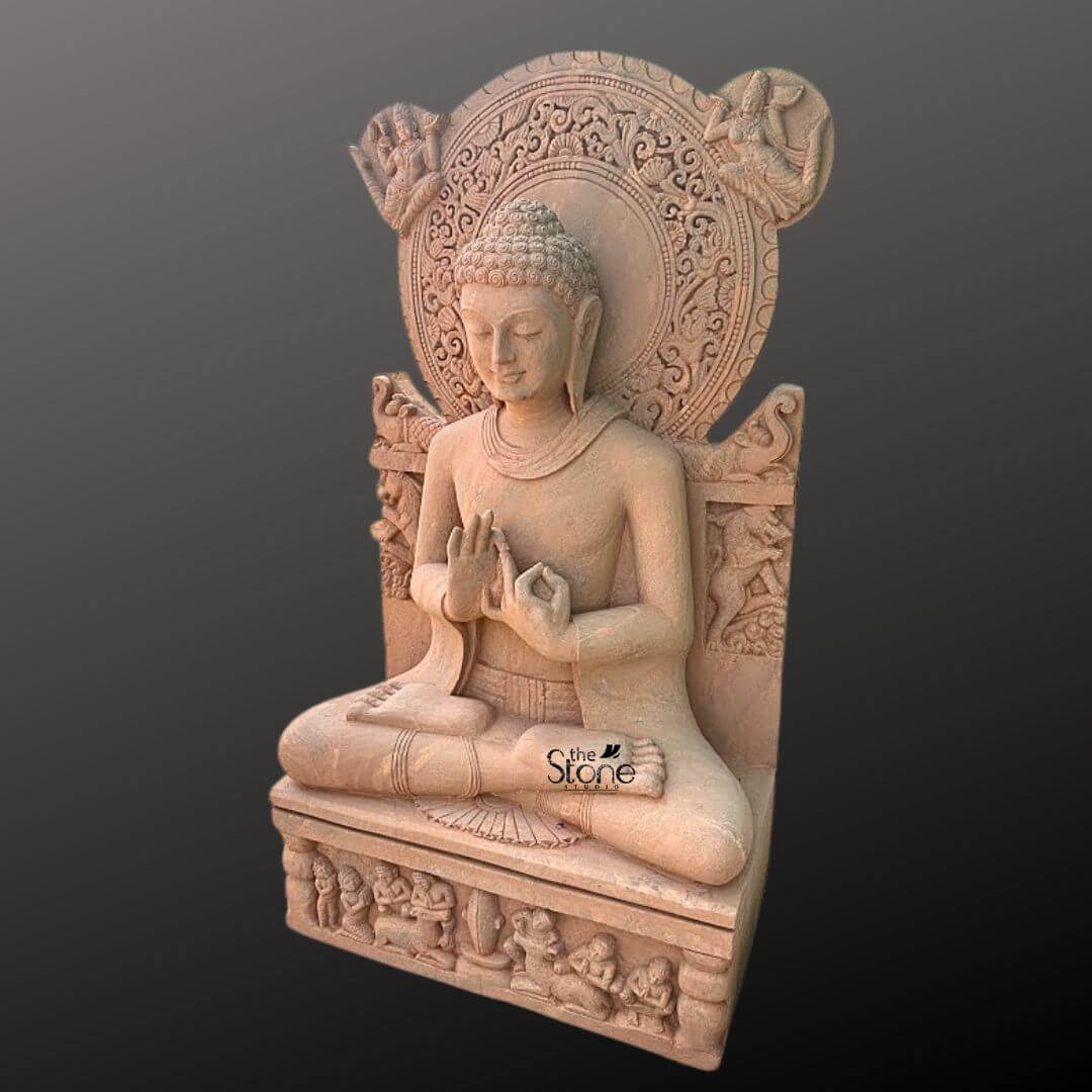 Sandstone Buddha Statue in Dharmachakra Mudra 5ft 2 A three-quarter view photograph of a magnificent 5-foot tall sandstone Buddha statue seated in the lotus position on a decorative pedestal against a dark gradient background. The statue is meticulously carved from warm reddish-brown sandstone showcasing the natural texture of the stone. The Buddha is depicted in the Dharmachakra Mudra with his hands held at chest level forming the Wheel of Dharma gesture. His eyes are gently closed and he wears a serene expression dressed in traditional finely draped robes. The attention to detail is exceptional with delicate folds in the garment and subtle facial features. Rising prominently behind the Buddha is a large and exquisitely ornate halo or prabhamandala which is the central focus of this piece. This halo is circular and features intricate relief carvings of floral patterns, celestial figures and mythical creatures adding to the statue's divine and majestic appearance. The backrest of the seat is also adorned with carvings of elephants and other auspicious symbols. The craftsmanship of the halo is highly detailed demonstrating the skill of the sculptors in creating a complex and beautiful work of religious art that enhances the presence of the main figure. The statue is seated upon a robust rectangular pedestal which is equally detailed with carved panels depicting rows of devotees and other figures in reverent poses. The overall composition highlights the monumental scale and spiritual significance of the Buddha Stone Statue with Ornate Halo. The three-quarter perspective allows for a clear view of both the statue's front and side profiles showcasing its three-dimensional depth and the elaborate carvings on the halo and pedestal. The lighting is soft and directional accentuating the textures and details of the sandstone carving.