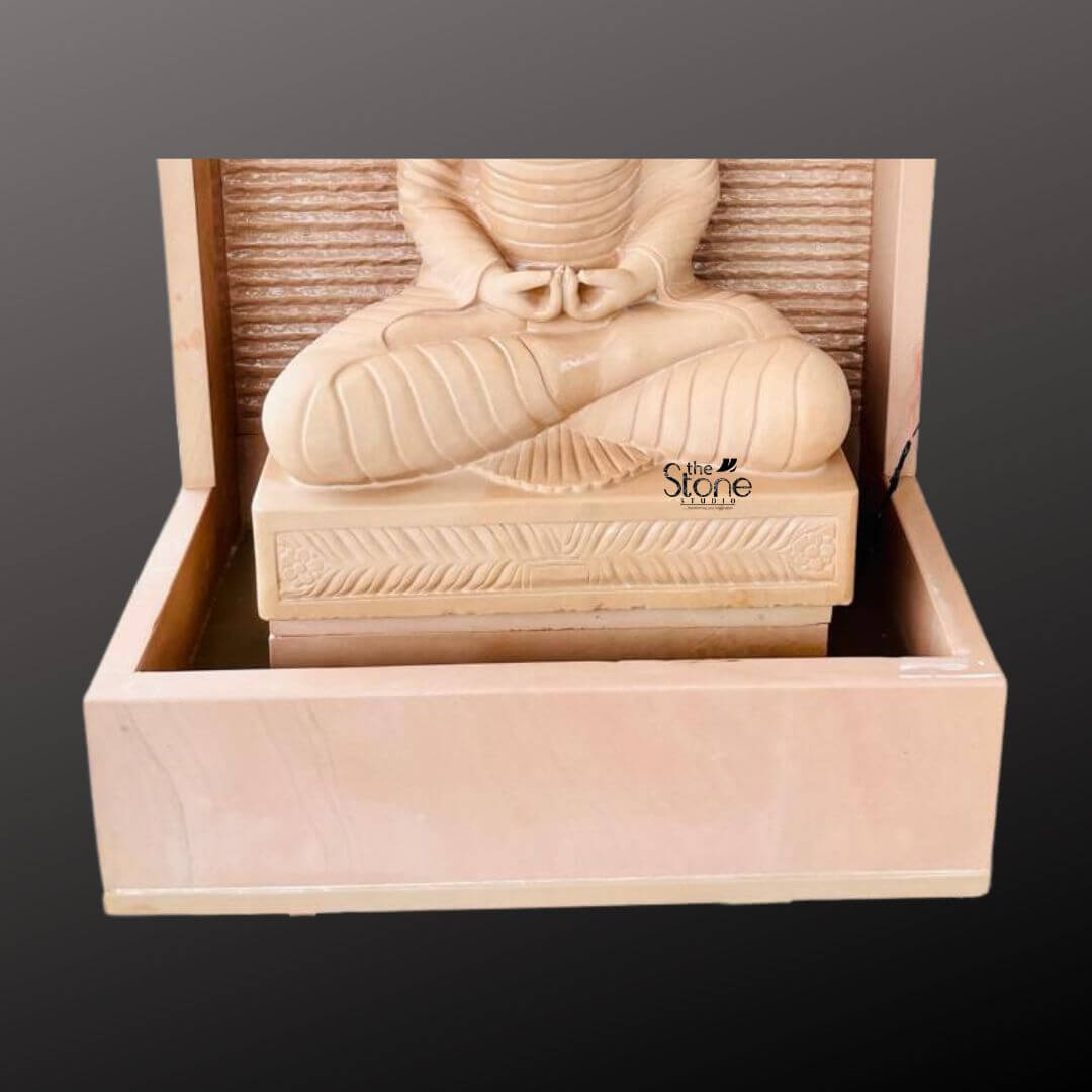 Outdoor Buddha Stone Water Fountain 4.5ft 5 A four-and-a-half-foot tall Buddha statue sits in a traditional meditative pose serving as the serene centerpiece of an elegant garden water fountain. The entire fountain structure including the statue is hand-carved from beautiful light beige-to-grey off-white sandstone exhibiting a natural textured porous surface that enhances its organic earthy feel. The Buddha is depicted seated with legs crossed in a full lotus position on a raised pedestal with hands resting in the lap in the dhyana mudra of deep contemplation. The flowing folds of the monastic robes are subtly rendered showcasing the exquisite craftsmanship and reverence for traditional iconography. The statue is enclosed within a monolithic frame-like sandstone structure creating a stunning wall-fountain design. Water is subtly distributed to flow like a gentle curtain down the textured horizontally-ribbed back panel directly behind the Buddha pooling into the large monolithic rectangular basin at the base. The sound of the cascading water adds a tranquil multi-sensory dimension to the visual stillness of the statue creating a peaceful and meditative atmosphere. The warm earthy hue of the sandstone contrasts beautifully with the environment making the statue pop and highlighting its intricate details and substantial presence which commands attention as a piece of sacred art. This four-and-a-half-foot Buddha Fountain Off White Sandstone Statue is an ideal illustration for an article discussing Garden Buddha Fountain demonstrating how such a piece can transform a garden patio or courtyard into a peaceful sanctuary. Its large scale ensures it becomes a commanding focal point while the durable sandstone construction makes it suitable for enduring outdoor elements as a long-lasting garden ornament. The combination of traditional sacred art with the gentle movement of water embodies a sense of harmony and spirituality perfect for creating a dedicated space for meditation reflection and aesthetic appreciation in any outdoor living area. The detailed carving and harmonious integration of elements highlight its value as both a decorative and a meaningful addition to a modern landscape.