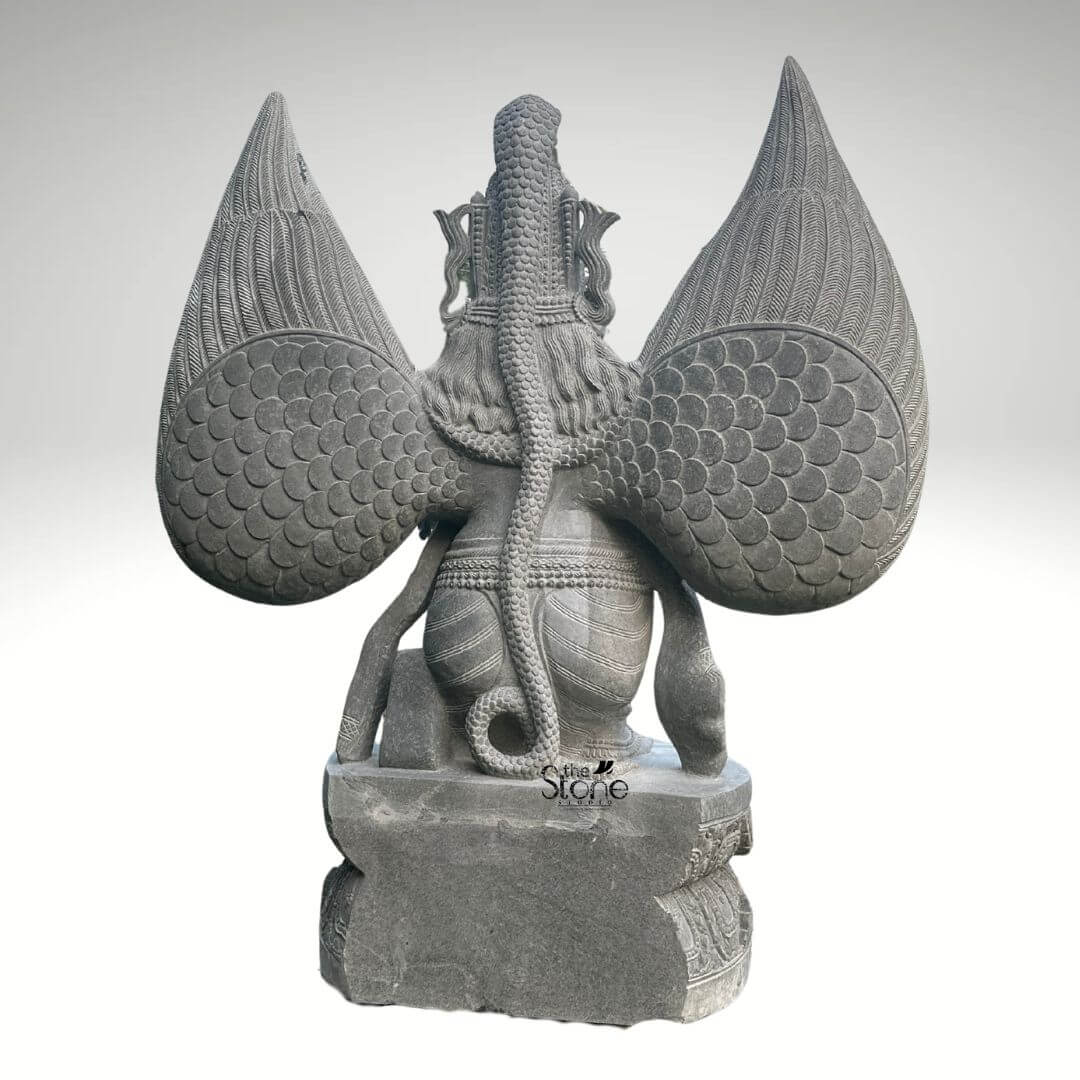 Grey Stone Garuda Statue 5.5ft 2 A detaile rear-facing photograph captures a majestic 5.5-foot-tall Garuda Garden Statue meticulously hand-carved from a single block of natural grey stone. The statue presents a powerful and complex composition from behind showcasing the intricate artistry of traditional stone carving. The central figure is the mythical bird-deity Garuda depicted with large folded wings that rise prominently their surface textured with overlapping, scale-like feathers that catch the light. A long textured serpent is coiled dramatically along the entire length of Garuda's spine and tail its scales and segmented body rendered with fine precision creating a striking contrast with the larger feather patterns. Garuda's form including his broad shoulders and defined back muscles is revealed beneath the coiled Naga and his lower body is draped in simple carved garments.The Garuda statue is elevated standing upon a robust carved rectangular stone pedestal base. The pedestal itself is adorned with decorative reliefs on its visible sides adding to the overall grandeur of the sculpture. The grey stone material has a natural slightly matte finish with subtle organic color variations and crystalline flecks emphasizing its authenticity and durability as a garden sculpture designed for outdoor placement. The carving exhibits a high level of detail from the individual feather points to the segmented body of the Naga reflecting the skill and patience of the master artisan who created it.This five-and-a-half-foot grey stone Garuda Garden Statue is an exceptional example of traditional Indian stonework making it a perfect subject for an article discussing garden sculptures. Its large size and detailed craftsmanship ensure it will serve as a commanding and spiritual focal point in any garden courtyard or landscaped area. The symbolic significance of Garuda as a protector and the celestial mount of Lord Vishnu adds a layer of cultural and religious depth. The rear view offers a unique and detailed perspective of the statue's complex iconography particularly the dramatic depiction of Garuda with the Naga which is a key element of his legend. The durable grey stone guarantees its longevity and aesthetic appeal for years to come.