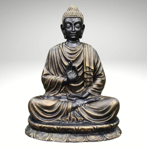 A large 5 feet fibre Buddha statue is shown in a clean product-style image against a soft light grey background allowing the sculpture to stand out clearly as the main focus. The Buddha is seated cross-legged on a layered lotus pedestal with one hand raised in a graceful teaching or blessing gesture and the other resting calmly in the lap. The face has a serene expression with gently closed eyes elongated earlobes and softly defined features that convey peace meditation and inner calm. The statue’s hair is formed in textured curls with a light golden finish creating contrast with the darker face and adding visual richness to the overall design. The fibre Buddha statue has a striking black and antique gold finish that gives it a refined timeless appearance. Flowing robe folds drape naturally across the shoulders chest arms and legs with metallic gold highlights accentuating the contours and sculpted details. The broad lotus base features repeated petal carvings around the bottom edge grounding the seated figure and enhancing the spiritual symbolism of the piece. The balanced posture smooth sculpting and subtle metallic sheen make the statue appear both devotional and decorative suitable for elegant interiors as well as spiritual settings. This image connects perfectly to an article about a Large Fibre Buddha Statue by clearly showcasing the size craftsmanship and decorative appeal of a 5 feet Buddha fibre statue. It presents the sculpture as an ideal choice for meditation rooms living spaces spiritual corners wellness centres entrance areas or garden-inspired décor where a larger statement piece is desired. The calm expression lotus seat antique finish and detailed robe work highlight how a large fibre Buddha statue can bring serenity mindfulness and sophisticated spiritual charm to home décor or commercial spaces.