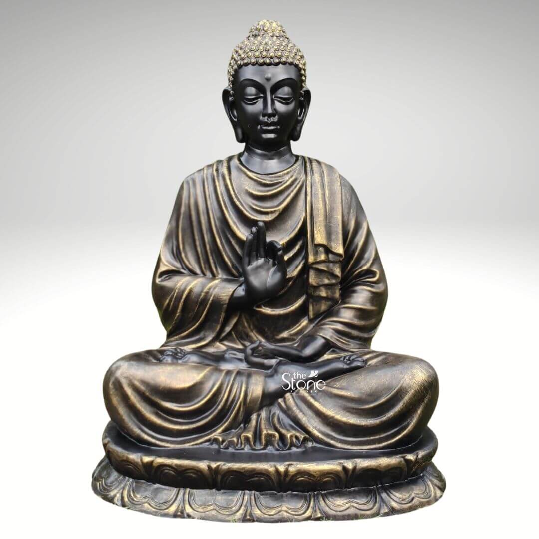 Large Fibre Buddha Statue 5ft 1 A large 5 feet fibre Buddha statue is shown in a clean product-style image against a soft light grey background allowing the sculpture to stand out clearly as the main focus. The Buddha is seated cross-legged on a layered lotus pedestal with one hand raised in a graceful teaching or blessing gesture and the other resting calmly in the lap. The face has a serene expression with gently closed eyes elongated earlobes and softly defined features that convey peace meditation and inner calm. The statue’s hair is formed in textured curls with a light golden finish creating contrast with the darker face and adding visual richness to the overall design. The fibre Buddha statue has a striking black and antique gold finish that gives it a refined timeless appearance. Flowing robe folds drape naturally across the shoulders chest arms and legs with metallic gold highlights accentuating the contours and sculpted details. The broad lotus base features repeated petal carvings around the bottom edge grounding the seated figure and enhancing the spiritual symbolism of the piece. The balanced posture smooth sculpting and subtle metallic sheen make the statue appear both devotional and decorative suitable for elegant interiors as well as spiritual settings. This image connects perfectly to an article about a Large Fibre Buddha Statue by clearly showcasing the size craftsmanship and decorative appeal of a 5 feet Buddha fibre statue. It presents the sculpture as an ideal choice for meditation rooms living spaces spiritual corners wellness centres entrance areas or garden-inspired décor where a larger statement piece is desired. The calm expression lotus seat antique finish and detailed robe work highlight how a large fibre Buddha statue can bring serenity mindfulness and sophisticated spiritual charm to home décor or commercial spaces.