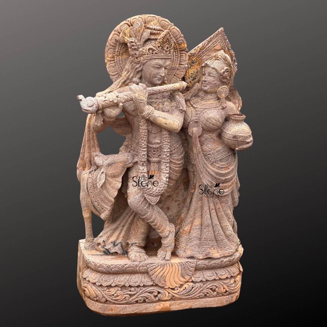 Radha Krishna Stone Statue with Cow 4ft 6 A magnificent 4-foot Lord Krishna with Radha and Cow Stone Statue intricately carved from warm reddish-brown sandstone stands gracefully against a dark gradient background radiating divine love and harmony. The statue vividly depicts Lord Krishna with Radha in a loving standing pose. Krishna distinguished by his elaborate crown and serene expression holds a flute to his lips poised as if playing a melodious tune. Radha stands gracefully beside him adorned with a similar crown and traditional attire her gaze fixed on Krishna while she carries a pot of water or butter symbolizing her devotion and nurturing spirit. This detailed carving beautifully captures their divine romance and pastoral setting. The craftsmanship is exquisite with intricate details defining their elaborate crowns delicate jewelry and flowing traditional garments. The sandstone's natural texture and subtle variations in color enhance the antique feel of the sculpture bringing out the tender expressions on their faces and the intricate patterns of their attire. A halo-like circular aureole with ornate patterns frames Krishna's head further emphasizing his divine presence. A key element central to the article's title is the inclusion of a small docile cow depicted near Krishna's feet symbolizing his role as a protector and caretaker of cattle and adding to the pastoral charm and traditional iconography. The entire ensemble rests on a multi-tiered intricately carved pedestal adorned with lotus petal designs and other traditional motifs providing a stable and dignified foundation. The depth and detail of the carving across the entire 4-foot statue are remarkable showcasing the artistry of the piece. This Sandstone Lord Krishna with Radha and Cow Stone Statue is an exquisite example of religious artistry designed to bring blessings love and aesthetic beauty to any home or temple making it an ideal focal point for devotion perfectly aligning with an article focusing on such charming and symbolically rich divine sculptures.