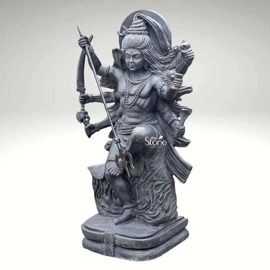 2 Feet Tandava Shiva Statue 7 A full-body studio photograph of a magnificent 2-foot tall Lord Shiva Tandava Murti masterfully hand-carved from a single block of dense polished black stone. The statue captures Lord Shiva in the dynamic and powerful Ananda Tandava pose the dance of cosmic bliss set upon a multi-tiered lotus pedestal. Shiva is portrayed with ten arms fanned out to convey movement holding various divine attributes including a trident and a damaru drum. His matted hair is piled high adorned with a crescent moon and a serpent and flares out dramatically emphasizing the energy and rhythm of his celestial dance. The intricate details of the carving from the delicate folds of Shiva's garment to the fierce yet serene expression on his face and the form of the demon Muyalakan subdued beneath his foot showcase the exquisite craftsmanship involved in creating this handcrafted piece. The black stone used for the statue has a deep rich hue with a subtle waxy luster giving it a powerful and reverent presence that complements the traditional iconography. The ten arms are arranged with precision some raised in gestures of protection and blessing others holding attributes like a conch shell a fire pot and a scripture. Shiva's right leg is raised bent at the knee while his left leg is planted firmly on the demon Muyalakan who lies subdued beneath his foot symbolizing the triumph of knowledge over ignorance. The dynamism of the dance is conveyed through the arching of his body and the intricate arrangement of his limbs creating a sense of controlled power and divine ecstasy. This 2-foot black stone Tandava Shiva Murti stands as a perfect embodiment of Indian temple art and a meaningful centerpiece for any sacred space or home altar. Its compact size allows for placement where its intricate details and spiritual energy can be admired. The dark monolithic stone gives it a timeless quality while the powerful iconography of the Tandava pose evokes a sense of cosmic rhythm creation and destruction making it an ideal choice for anyone seeking to bring a touch of Eastern spirituality and artistic heritage into their environment. The photograph presents the statue against a clean neutral white background ensuring the focus remains entirely on the form texture and spiritual significance of the black stone sculpture.