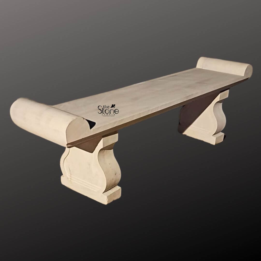 Sandstone Garden Bench 6ft 4 A six-foot-long Natural Sandstone Bench stands against a seamless dark grey studio background showcasing its elegant classical design. The bench is hand-carved from authentic light beige sandstone exhibiting a beautifully textured porous surface that adds an authentic rustic charm. Its long flat seat is supported by two substantial decoratively sculpted legs. These legs feature a graceful S-curve or hourglass profile resting on sturdy block-like bases that anchor the entire piece. The craftsmanship is evident in the smooth yet hand-hewn finish of the stone which catches the light and highlights its natural variations in color and texture from pale cream to subtle warm brown tones. The design of this sandstone bench is distinctly traditional inspired by historical European garden furniture. The seat itself is not plain it terminates at both the left and right ends with large perfectly formed scrolled volutes or rolled ends. These sculptural elements not only provide comfortable armrests but also define the bench's aesthetic lending it a sophisticated and timeless appeal. The overall form is balanced and substantial suggesting durability and a permanent place within a garden landscape. The stone appears heavy and solid capable of withstanding the elements for decades. This six-foot sandstone bench is the perfect embodiment of a functional and decorative Natural Sandstone Bench. Its generous length provides ample seating for multiple people while its robust stone construction makes it an ideal choice for outdoor settings like patios courtyards or nestled within garden pathways. The light neutral color of the sandstone harmonizes beautifully with surrounding greenery flowers and other natural elements. This bench is not just a piece of furniture it is a sculptural addition to a garden designed to offer a comfortable and contemplative spot to rest and enjoy the beauty of the outdoors.