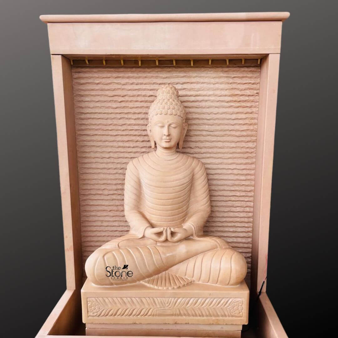 Outdoor Buddha Stone Water Fountain 4.5ft 9 A magnificent hand-carved four-and-a-half-foot tall Seated Buddha Fountain in Off White Sandstone sits as the serene centerpiece of a water feature presented against a dark grey background. The entire fountain structure including the statue is crafted from beautiful light beige-to-grey sandstone exhibiting a natural textured porous surface that enhances its organic earthy feel. The Buddha is depicted in a traditional seated meditative pose on a raised lotus pedestal with legs crossed in a full lotus position and hands resting in the lap in the dhyana mudra of deep contemplation. His facial expression is calm and compassionate with downcast eyes a gentle smile and tightly curled hair leading to a cranial ushnisha all rendered with exquisite craftsmanship and flowing yet subtle carved folds of his monastic robes. The statue is enclosed within a monolithic frame-like sandstone structure creating a stunning wall-fountain design. Water is subtly distributed to flow like a gentle curtain down the textured horizontally-ribbed back panel directly behind the Buddha pooling into the large monolithic rectangular basin at the base. The sound of the cascading water adds a tranquil multi-sensory dimension to the visual stillness of the statue creating a peaceful and meditative atmosphere. The warm, earthy hue of the sandstone contrasts beautifully with the cool dark background making the statue pop and highlighting its intricate details and substantial presence which commands attention as a piece of sacred art. This four-and-a-half-foot Buddha Fountain Off White Sandstone Statue is an ideal illustration for an article discussing Seated Buddha Fountain in Off White Sandstone demonstrating how such a piece can transform an indoor or outdoor space into a peaceful sanctuary. Its large scale ensures it becomes a commanding focal point while the durable sandstone construction makes it suitable for enduring outdoor elements as a long-lasting garden or patio ornament. The combination of traditional sacred art with the gentle movement of water embodies a sense of harmony and spirituality perfect for creating a dedicated space for meditation eflection and aesthetic appreciation in any living area. The detailed carving and harmonious integration of elements highlight its value as both a decorative and a meaningful addition to a modern landscape.