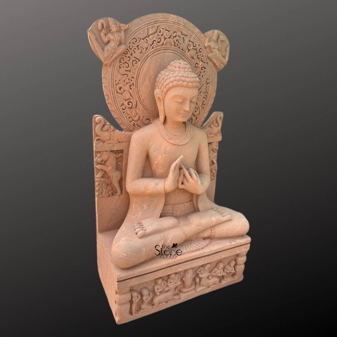 Sandstone Buddha Statue in Dharmachakra Mudra 5ft 6 A full-body studio photograph of a magnificent 5-foot tall seated Buddha statue expertly carved from warm reddish-brown sandstone. The statue is presented in a three-quarter profile against a neutral dark gray gradient background emphasizing its substantial presence and intricate details. The Buddha is seated in the traditional lotus position with both legs crossed and soles of the feet visible conveying a sense of profound tranquility and meditative calm. His hands are held at the chest level in the Dharmachakra Mudra the gesture of teaching and turning the wheel of Dharma with the thumb and index finger of both hands touching to form circles. The statue exhibits masterful craftsmanship with a serene facial expression downcast eyes and a gentle smile. The Buddha's hair is arranged in tight traditional curls leading up to the ushnisha and he has elongated earlobes. He is draped in simple finely-pleated robes that fall naturally over his body showcasing the natural texture and tactile quality of the sandstone. The overall carving is highly detailed from the subtle folds of the garment to the defined musculature of the torso highlighting the skill involved in creating this monumental piece of religious art. Rising prominently behind the seated Buddha is an elaborate intricately carved prabhamandala or halo. This circular aureole is adorned with complex relief patterns including stylized floral motifs celestial beings and mythical creaturs like makaras adding to the statue's divine aura. The backrest of the seat features further carvings of elephants reinforcing the grandeur of the sculpture. The statue rests upon a robust rectangular pedestal which is also decorated with carved panels depicting rows of devotees and other figures in reverent poses grounding the central figure within a narrative context. The three-quarter perspective allows for a comprehensive view of this significant handcrafted sandstone Buddha statue.
