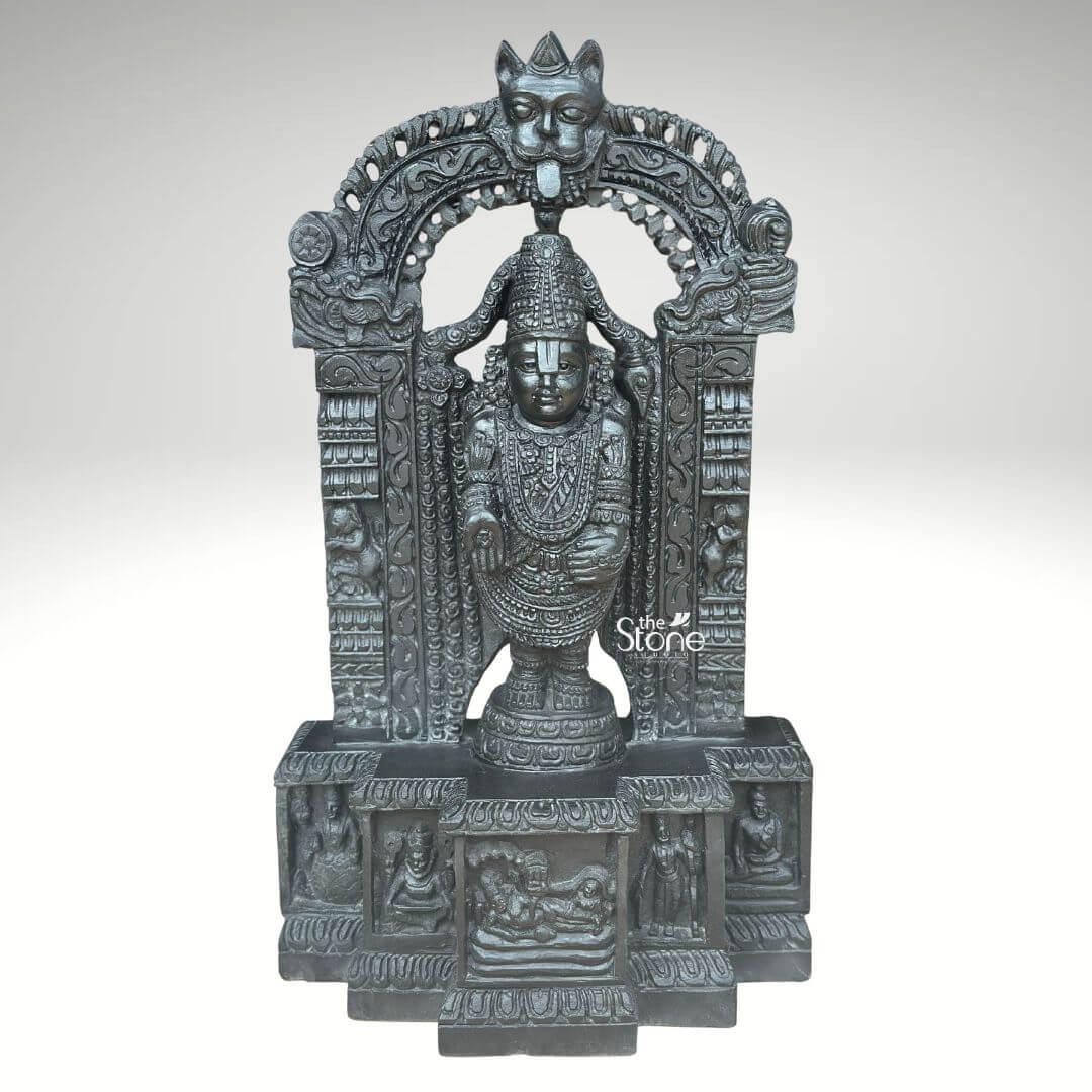 Sri Srinivasa Tirupati Balaji Statue 2.5ft 1 A detailed front-facing photograph presents a magnificent 2.5-foot-tall statue of Sri Srinivasa Tirupati Balaji meticulously hand-carved from a single block of dark dense blackstone. The statue depicts Lord Balaji standing in a samabhanga posture on a lotus pedestal which is itself supported by an ornate multi-tiered rectangular base. The dark stone has a deep matte finish that highlights the intricate sculptural details. Garuda the celestial eagle-mount is prominently carved at the apex of the elaborate prabhavali that frames the main deity. Below Garuda the arch is adorned with traditional floral and scrollwork motifs culminating in makara heads at the base of the pillars. Lord Balaji's divine form is richly adorned with finely carved traditional ornaments including multiple layered necklaces elaborate armbands bracelets and anklets. His forehead bears the distinct Vaishnava U-shaped tilak mark and his eyes are half-closed in a serene benevolent expression. His upper right hand holds a discus while his upper left hand holds a conch shell. His lower right hand is raised in the Varada mudra and his lower left hand rests gracefully on his hip. The fine detail extends to his draped clothing which is textured to resemble silk fabric held by a jeweled girdle. The rectangular base beneath the main figure is a work of art in itself featuring intricate bas-relief panels on its visible front face. The central panel depicts the reclining form of Lord Ranganatha resting on the serpent Adisesha attended by consorts. This central scene is flanked by smaller detailed carvings of sages devotees and other deities within architectural niches. The entire sculpture from the ornate pedestal to the top of the arch reflects the traditional South Indian Hoysala and Vijayanagara architectural styles. This 2.5-foot blackstone Tirupati Balaji statue is an exceptional piece of devotional art perfect for a home shrine or as a central exhibit capturing the spiritual essence and cultural heritage of the Venkateswara Temple. The photograph's clear focus on the statue's form and texture provides a comprehensive view for the viewer.