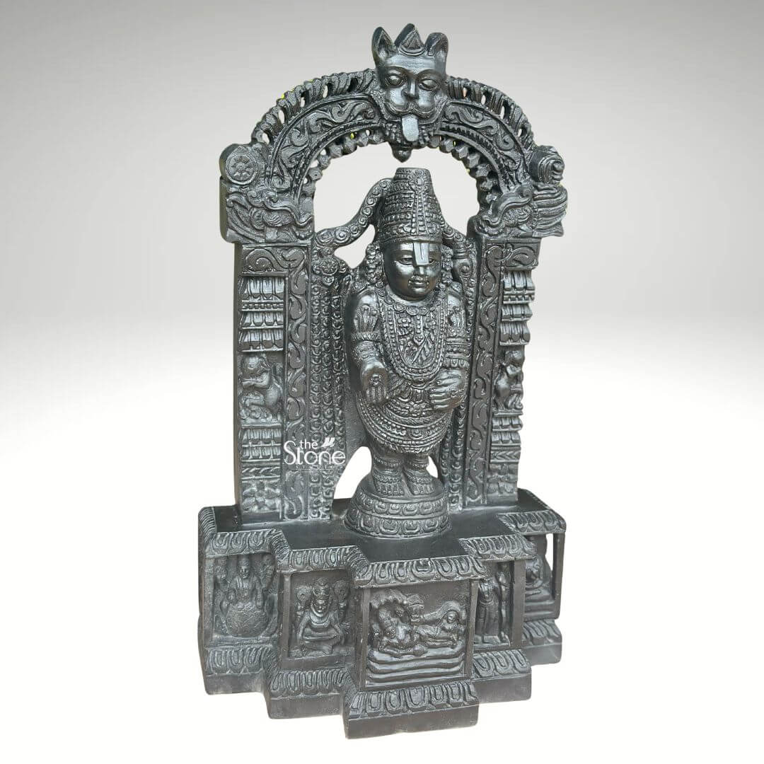 Sri Srinivasa Tirupati Balaji Statue 2.5ft 6 A detailed three-quarter view photograph captures a magnificent 2.5-foot-tall statue of Sri Venkateswara Swamy meticulously hand-carved from a single block of dark dense blackstone. The statue presents Lord Balaji standing in a samabhanga posture upon a lotus pedestal which is itself supported by an ornate multi-tiered rectangular base. The dark stone has a deep matte finish that accentuates the intricate sculptural details. Garuda the celestial eagle-mount is prominently carved at the apex of the elaborate prabhavali that frames the main deity. Below Garuda the arch is adorned with traditional floral and scrollwork motifs culminating in makara heads at the base of the pillars. Lord Balaji's divine form is richly adorned with finely carved traditional ornaments including multiple layered necklaces, elaborate armbands, bracelets, and anklets. His forehead bears the distinct Vaishnava U-shaped tilak mark and his eyes are half-closed in a serene benevolent expression. His upper right hand holds a discus while his upper left hand holds a conch shell. His lower right hand is raised in the Varada mudra and his lower left hand rests gracefully on his hip. The fine detail extends to his draped clothing, which is textured to resemble silk fabric held by a jeweled girdle.The rectangular base beneath the main figure is a work of art in itself featuring intricate bas-relief panels on its visible front face. The central panel depicts the reclining form of Lord Ranganatha resting on the serpent Adisesha attended by consorts. This central scene is flanked by smaller, detailed carvings of sages devotees, and other deities within architectural niches. The entire sculpture from the ornate pedestal to the top of the arch reflects the traditional South Indian Hoysala and Vijayanagara architectural styles. This 2.5-foot blackstone statue is an exceptional piece of devotional art perfect for a home shrine or as a central exhibi capturing the spiritual essence and cultural heritage of the Venkateswara Temple. The photograph's clear focus on the statue's form and texture provides a comprehensive view for the viewer.