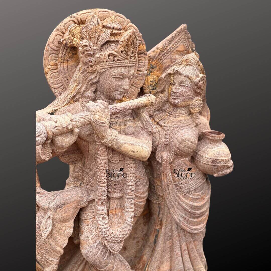 Radha Krishna Stone Statue with Cow 4ft 2 A close-up view of a magnificent 4-foot Standing Radha Krishna Stone Sculpture with Cow intricately carved from warm reddish-brown sandstone reveals the delicate artistry against a dark gradient background. The statue captures Lord Krishna and Radha in an intimate and loving standing pose. Krishna distinguished by his elaborate crown and serene expression holds a flute to his lips seemingly in the act of playing with his head gently tilted towards Radha. Radha stands gracefully beside him adorned with a similar crown and traditional attire her gaze fixed on Krishna while she carries a pot of water or butter in her hand. This detailed carving beautifully highlights their divine romance and interaction. The craftsmanship is exceptional with every intricate detail defining their elaborate crowns delicate jewelr and flowing traditional garments. The sandstone's natural texture and subtle variations in color enhance the antique feel of the sculpture bringing out the tender expressions on their faces and the intricate patterns of their attire. Krishna's halo-like circular aureole with ornate patterns is partially visible behind him emphasizing his divine presence. A key element central to the article's title is the depiction of a small docile cow near Krishna's feet symbolizing his role as a protector and caretaker of cattle and adding to the pastoral charm. The figures stand on a multi-tiered intricately carved pedestal adorned with lotus petal designs and other traditional motifs providing a stable and dignified foundation. The depth and precision of the carving across the entire 4-foot statue are remarkable showcasing the artistry of the piece. This Sandstone Standing Radha Krishna sculpture with its endearing depiction of a cow is an exquisite example of religious artistry designed to evoke feelings of love devotion and peace perfectly aligning with an article focusing on such charming and symbolically rich Radha Krishna statues.