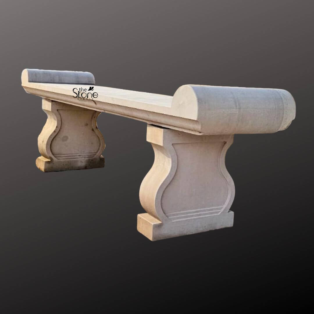 Sandstone Garden Bench 6ft 7 A six-foot-long sandstone garden bench stands against a seamless dark grey studio background showcasing its elegant classical design. The bench is hand-carved from natural light beige sandstone exhibiting a beautifully textured porous surface that adds an authentic rustic charm. Its long flat seat is supported by two substantial decoratively sculpted legs. These legs feature a graceful S-curve or hourglass profile resting on sturdy block-like bases that anchor the entire piece. The craftsmanship is evident in the smooth yet hand-hewn finish of the stone which catches the light and highlights its natural variations in color and texture from pale cream to subtle warm brown tones. The design of this sandstone bench is distinctly traditional inspired by historical European garden furniture. The seat itself is not plain it terminates at both the left and right ends with large perfectly formed scrolled volutes or rolled ends. These sculptural elements not only provide comfortable armrests but also define the bench's aesthetic lending it a sophisticated and timeless appeal. The overall form is balanced and substantial suggesting durability and a permanent place within a garden landscape. The stone appears heavy and solid capable of withstanding the elements for decades. This six-foot sandstone bench is the perfect embodiment of a functional and decorative Stone Garden Bench. Its generous length provides ample seating for multiple people while its robust stone construction makes it an ideal choice for outdoor settings like patios courtyards or nestled within garden pathways. The light neutral color of the sandstone harmonizes beautifully with surrounding greenery flowers and other natural elements. This bench is not just a piece of furniture it is a sculptural addition to a garden designed to offer a comfortable and contemplative spot to rest and enjoy the beauty of the outdoors.